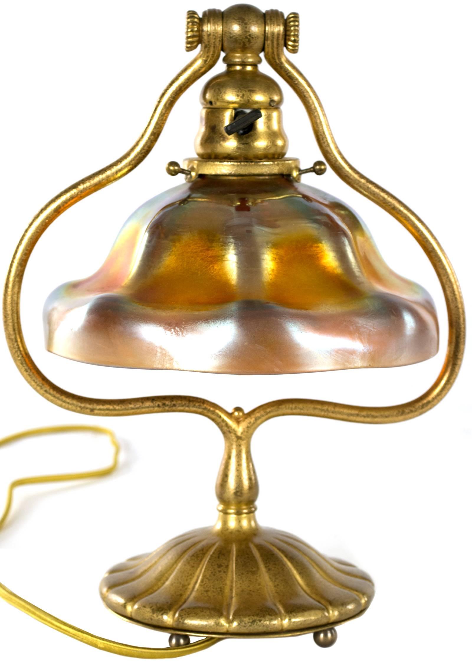 Exhibiting the quality and beauty of Tiffany's best work, the gilt bronze lamp body, in the shape of a harp holds an iridescent favrile glass lampshade. The base is stamped 