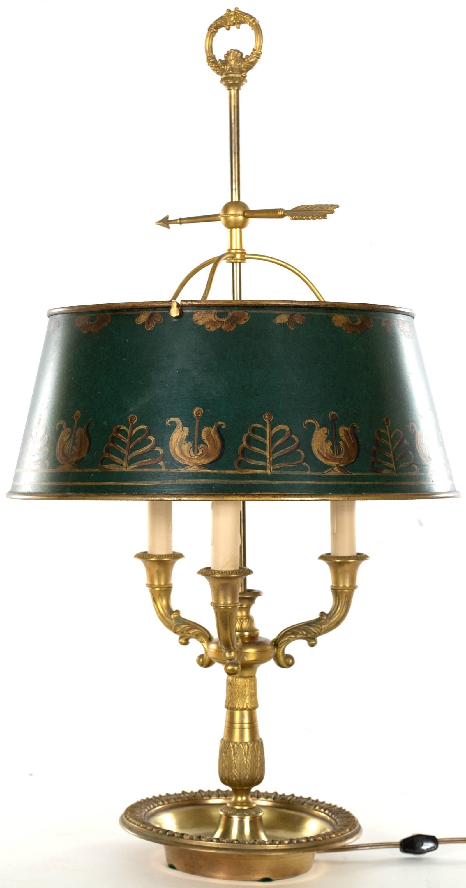 A charming table lamp in the form of a three-armed candelabra, with a green painted and gilt metal shade, made in England during the third quarter of the nineteenth century.