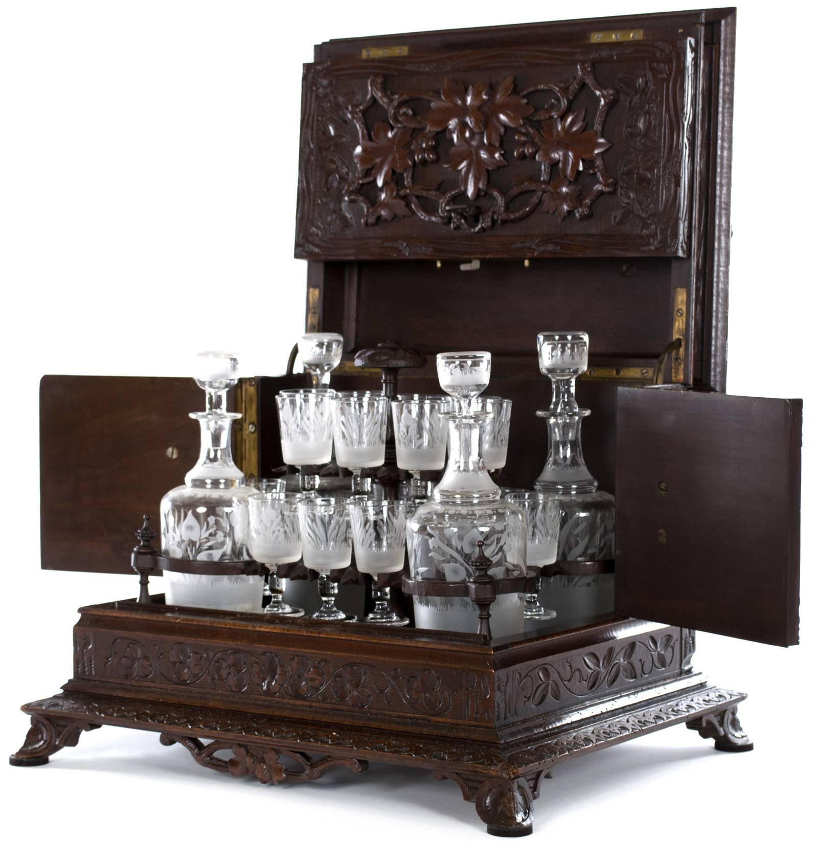 A carved walnut liquor cabinet, topped with a pair of quails surrounded by their clutch nestled in foliage, the handles on each side are in the form of bear heads, and the front is a beautifully rendered wreath of maple leaves and vines. The case