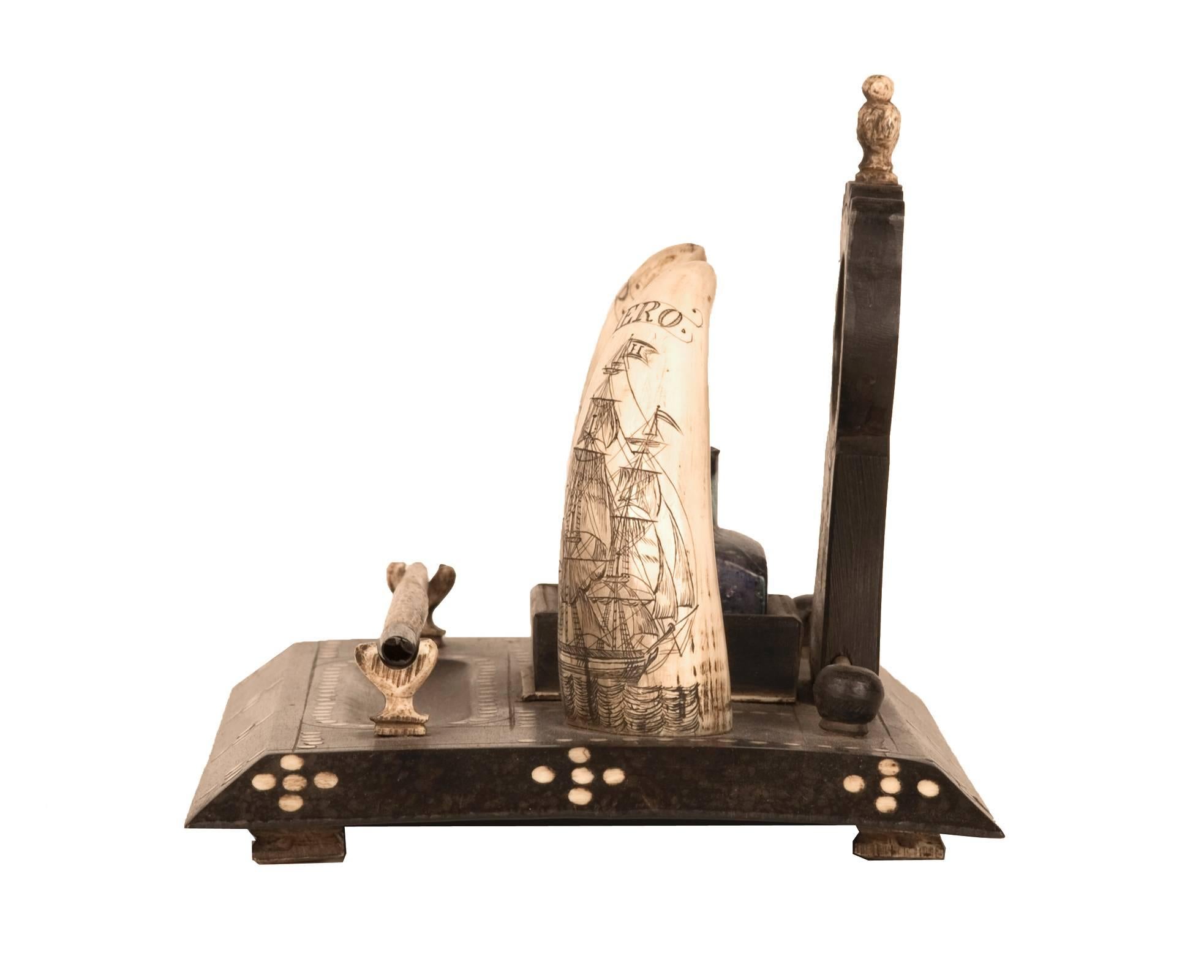 Ebonized baleen pen stand inlaid with a motif of tusk rounds, and scrimshaw whale teeth depicting a commemorative attribution to an American sailor. The teeth are engraved with the words “Ship” and “Hero”, and are accompanied with detailed