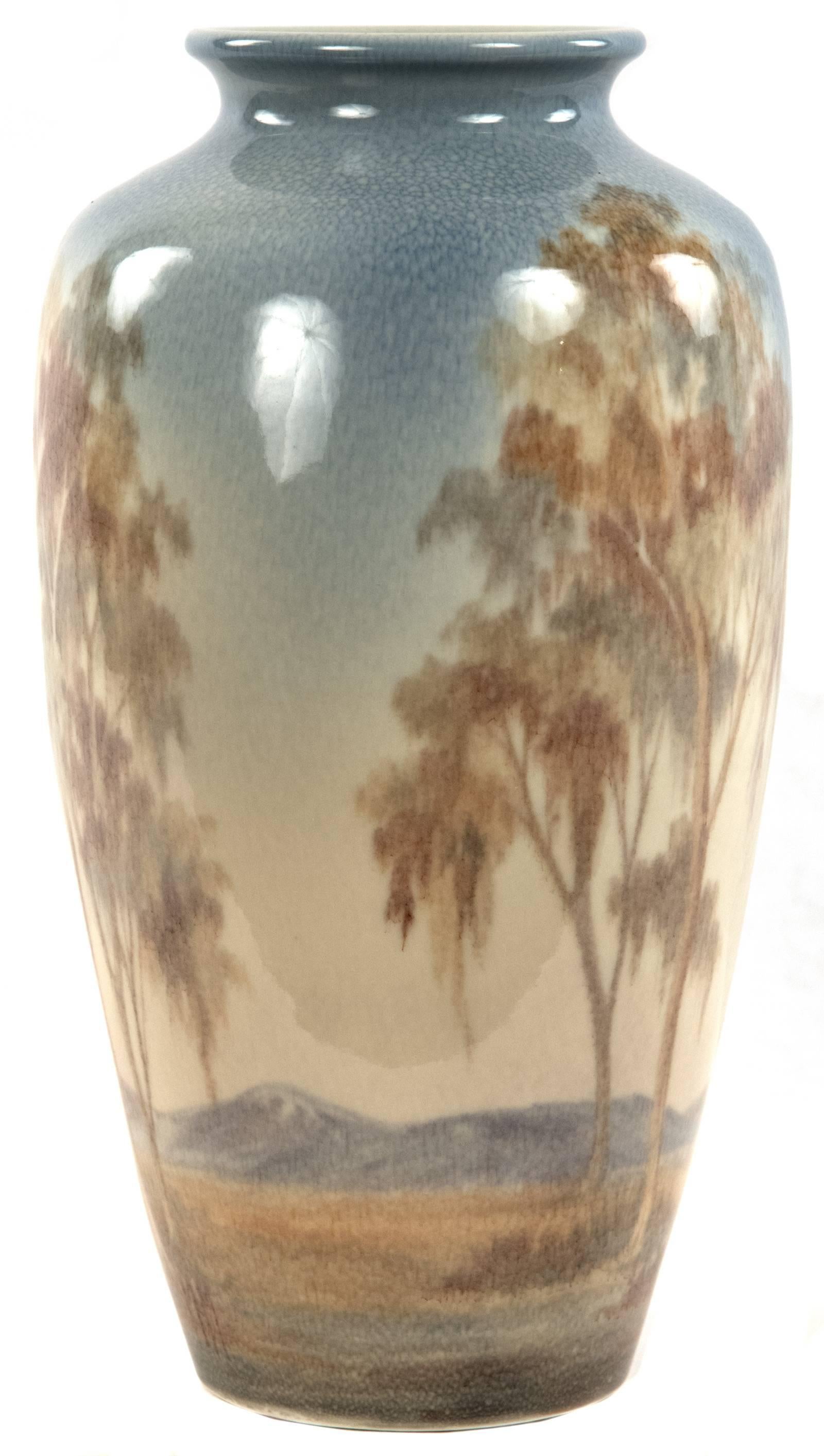 A tree-lined landscape with a mountain range in the distance is softly illustrated in a neutral palette of blue and brown glazes, and initialed 