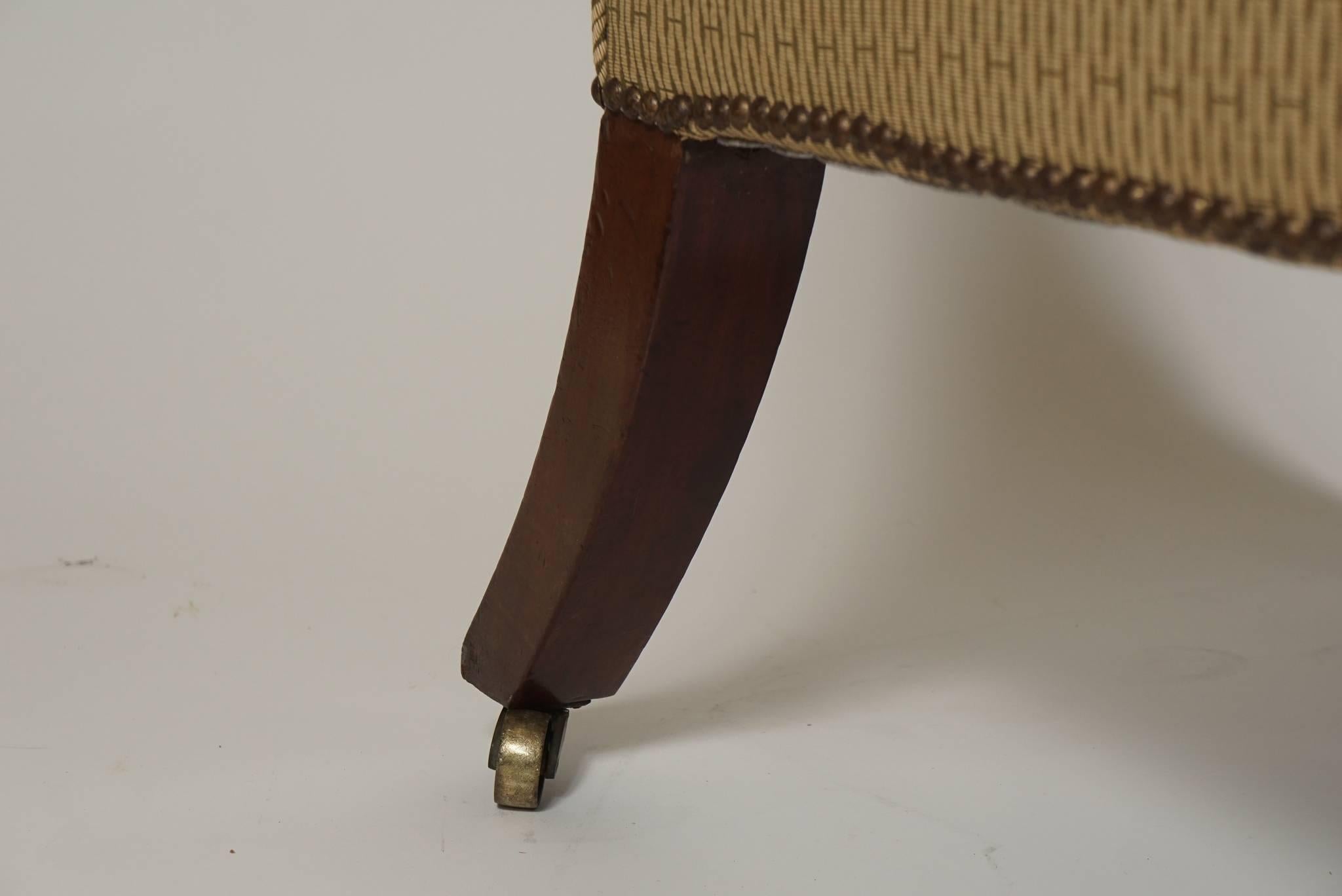 Une bergère ou un fauteuil inhabituel de la période Régence anglaise, avec des coins de dossier concaves et des motifs d'acanthe et de panneaux sculptés en acajou sur les extrémités des bras, les blocs d'angle et le rail de l'assise, avec des pieds