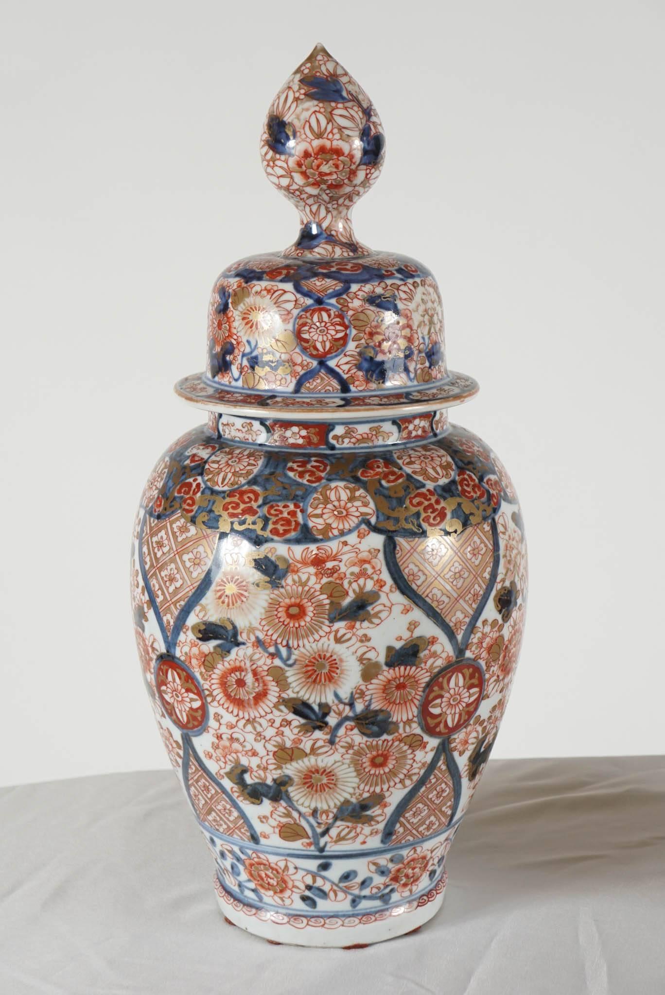 A beautiful pair of circa 1880 Japanese Imari porcelain covered jars in Edo style having globular bodies with foliate patterns painted in underglaze cobalt blue and overglaze iron red with allover gilded highlights. The high domed covers have