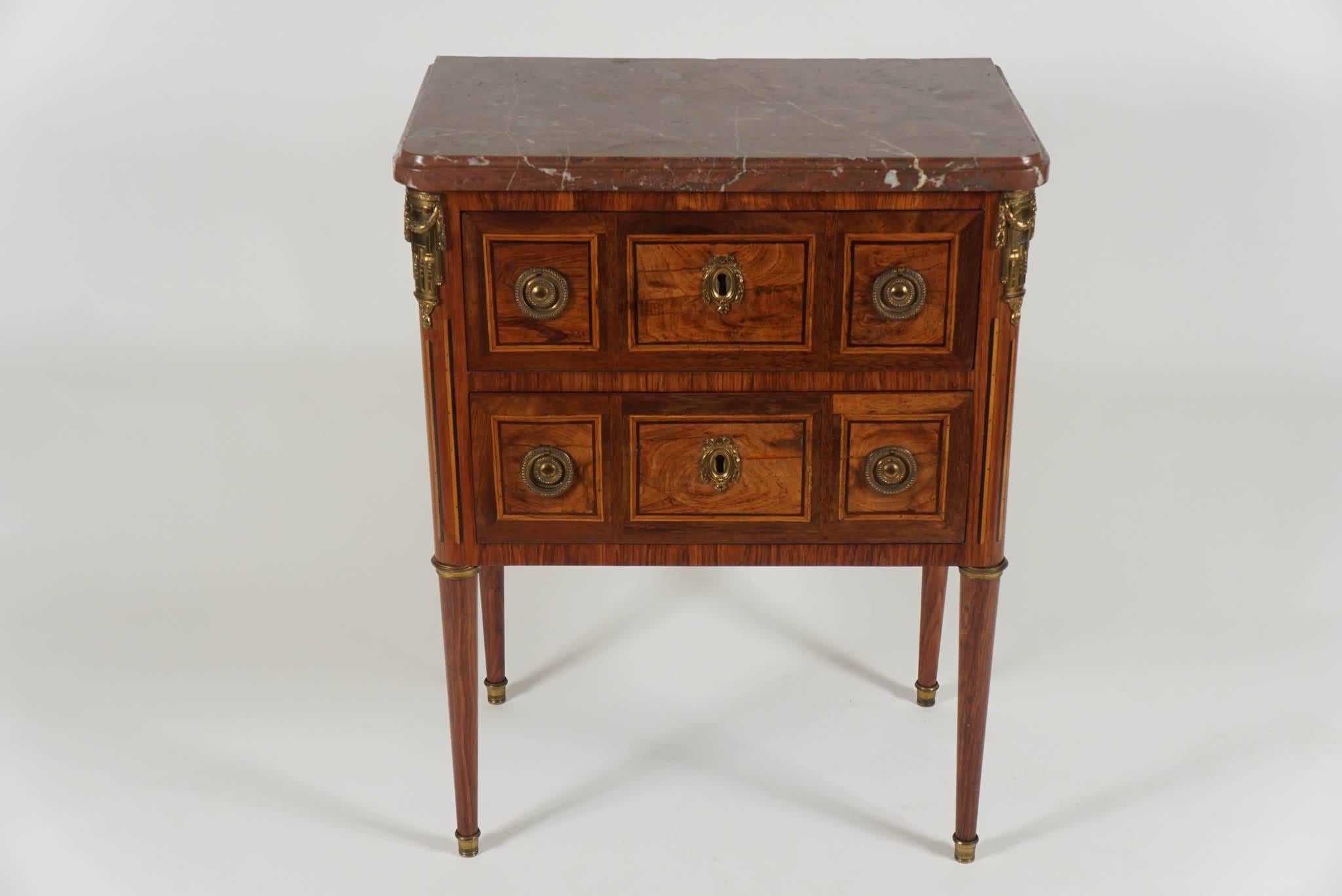 An exquisite, circa 1780, tulipwood, sycamore, kingwood, and ebony inlaid petite commode on stand by important Paris cabinetmaker Conrad Mauter (Maître 1777) having a Rosso Antico marble top above two locking drawers with geometric inlay and ormolu