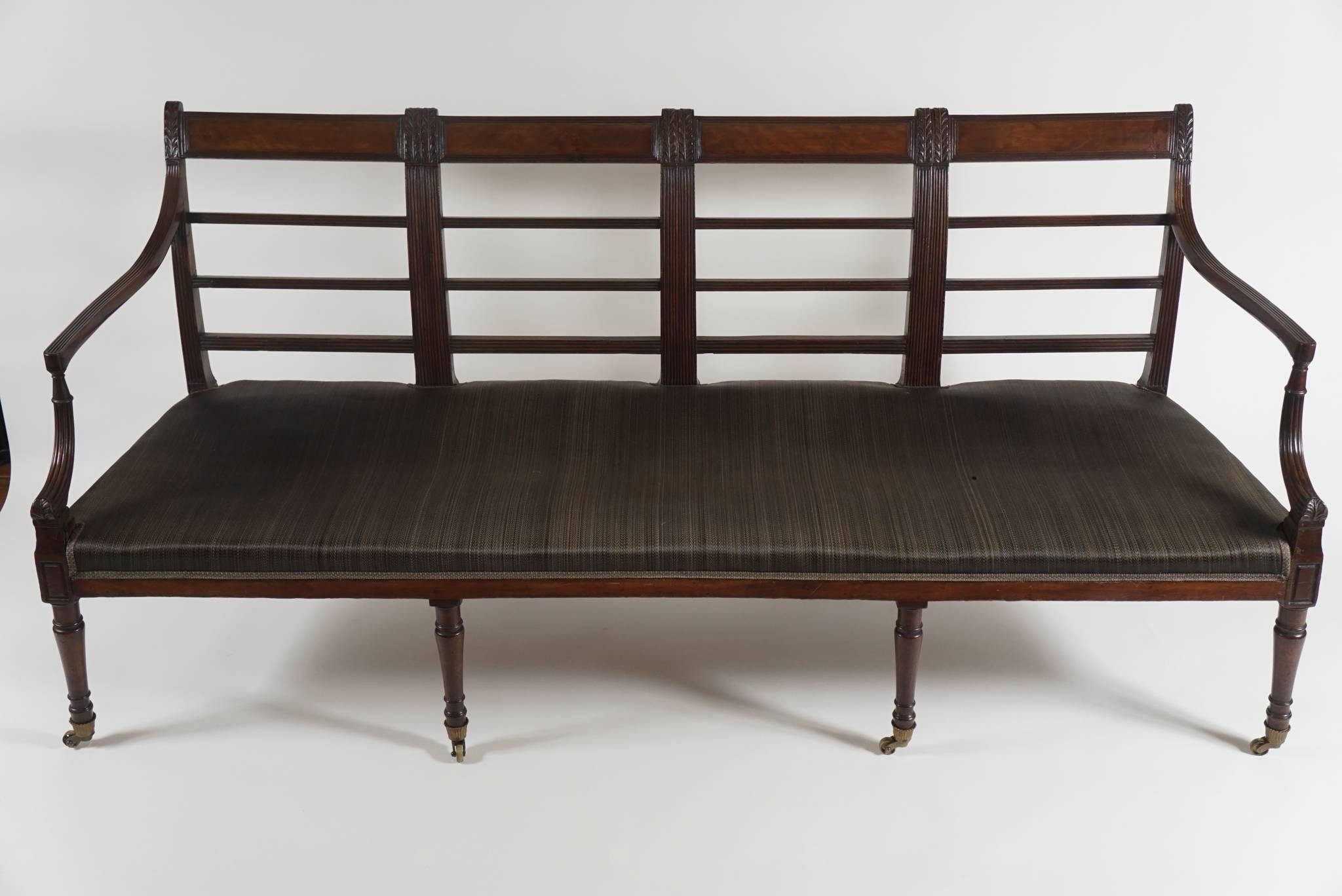 An unusual circa 1795, English George III period settee in Sheraton style of solid mahogany construction and rectangular form having four section 'ladder' back with inlaid tablet form crest-rail sections connecting reeded and acanthus carved