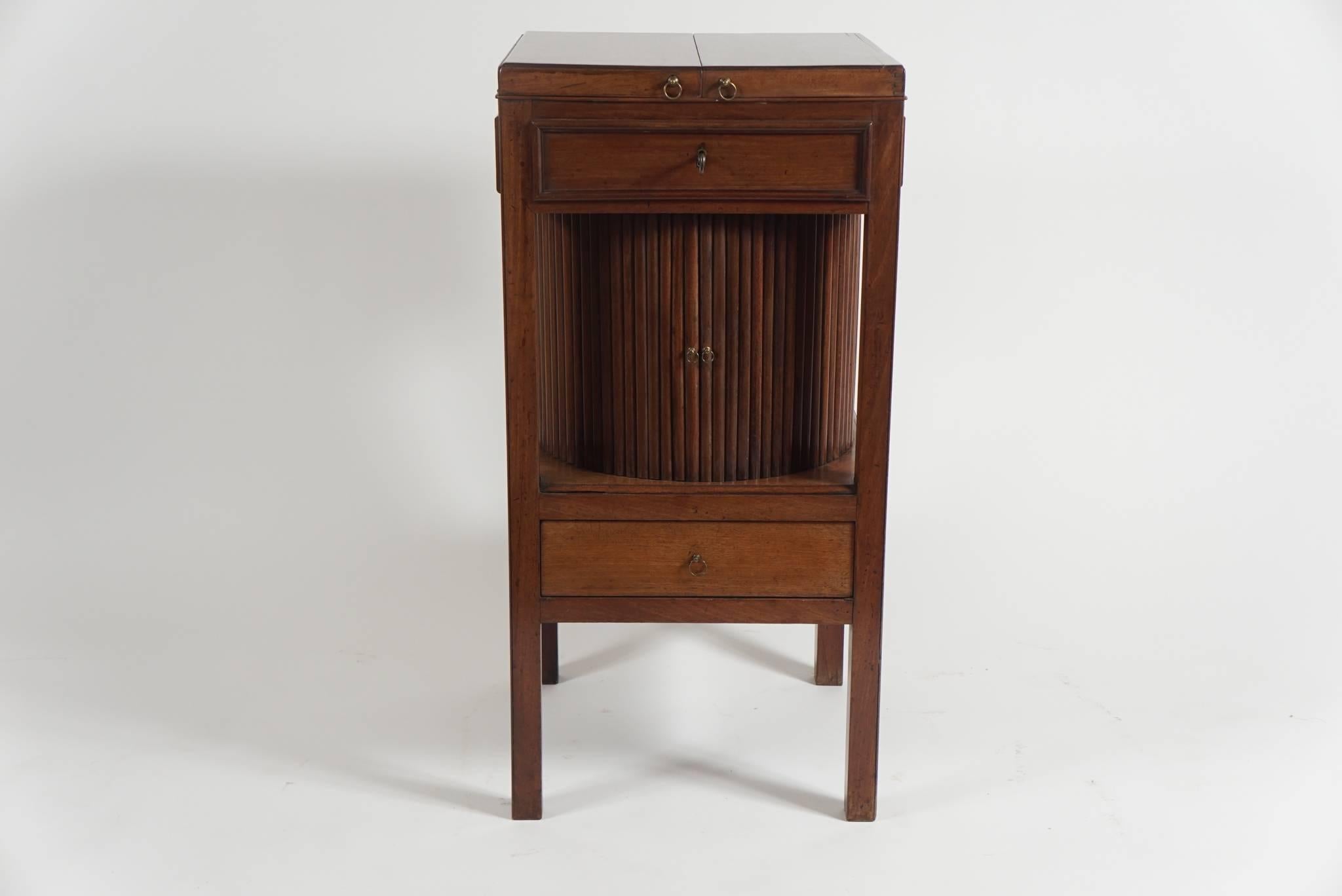 An elegant and unusual English George III period mahogany stand of rare form having 'butterfly' top revealing interior compartment above round center section with continuous reeded tambour slide surmounting lower drawer raised on four square