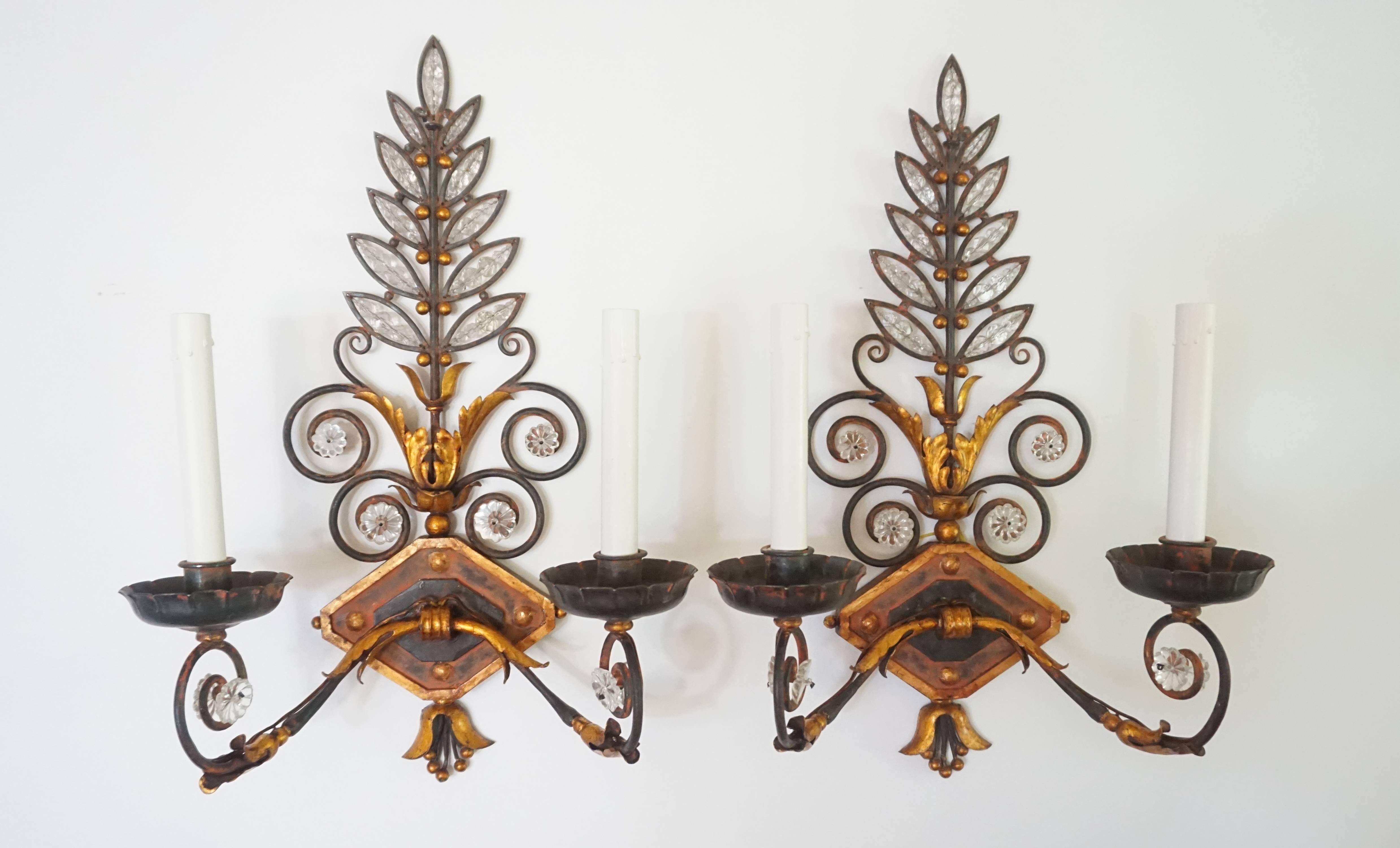 Pair of crystal and wrought iron two-light wall sconces attributed to Maison Baguès Paris, circa 1925, having parcel-gilt and red painted finish on open hand-wrought foliate and acanthus back-plates encrusted with flower-form and facet-cut bead