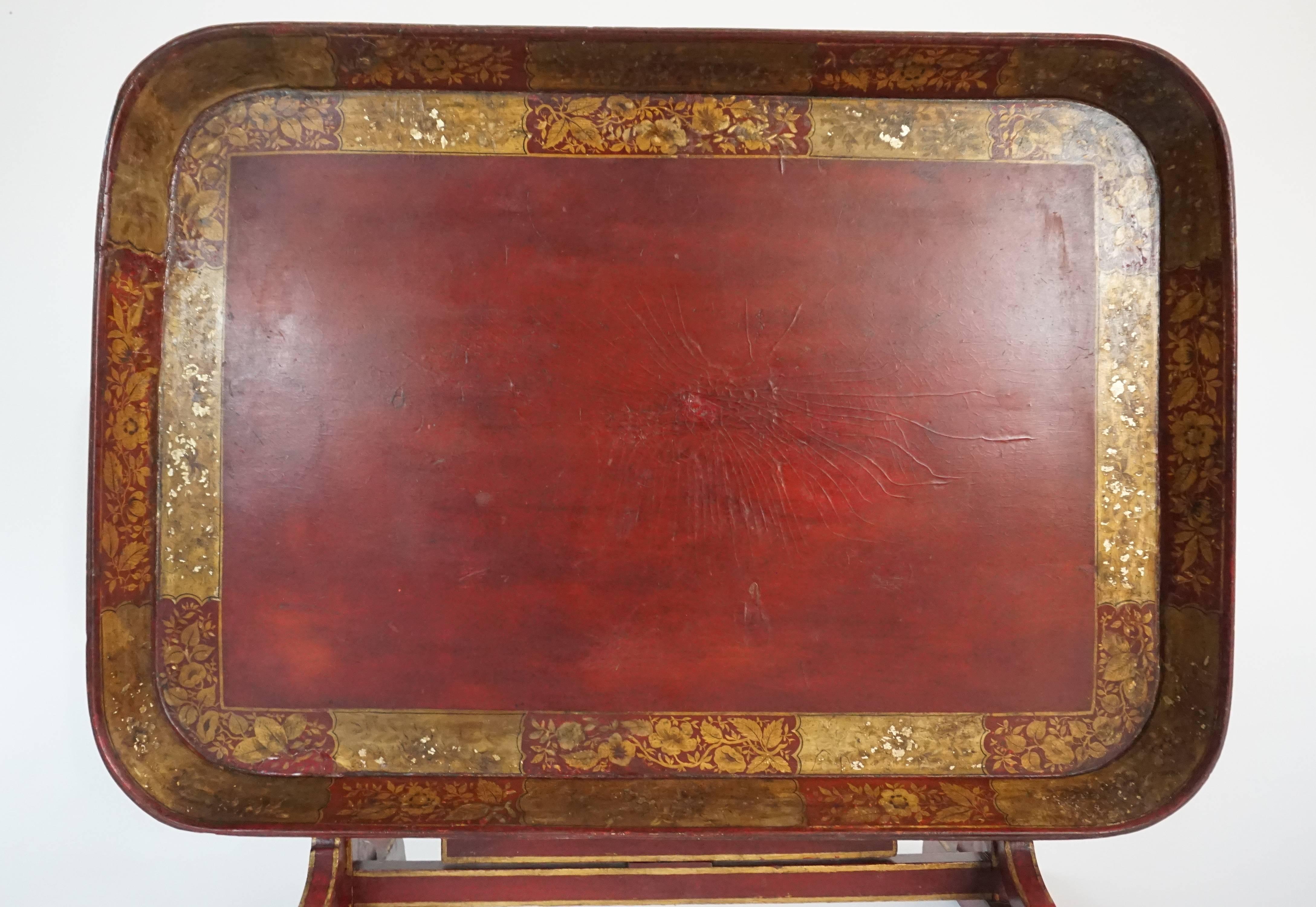 Very rare English Regency period, circa 1810, low table having cinnabar red papier ma^che´ tray top with gilt foliate geometric border on original parcel-gilt tilt-top trestle base Stand with central swiveling butterfly or gate support of