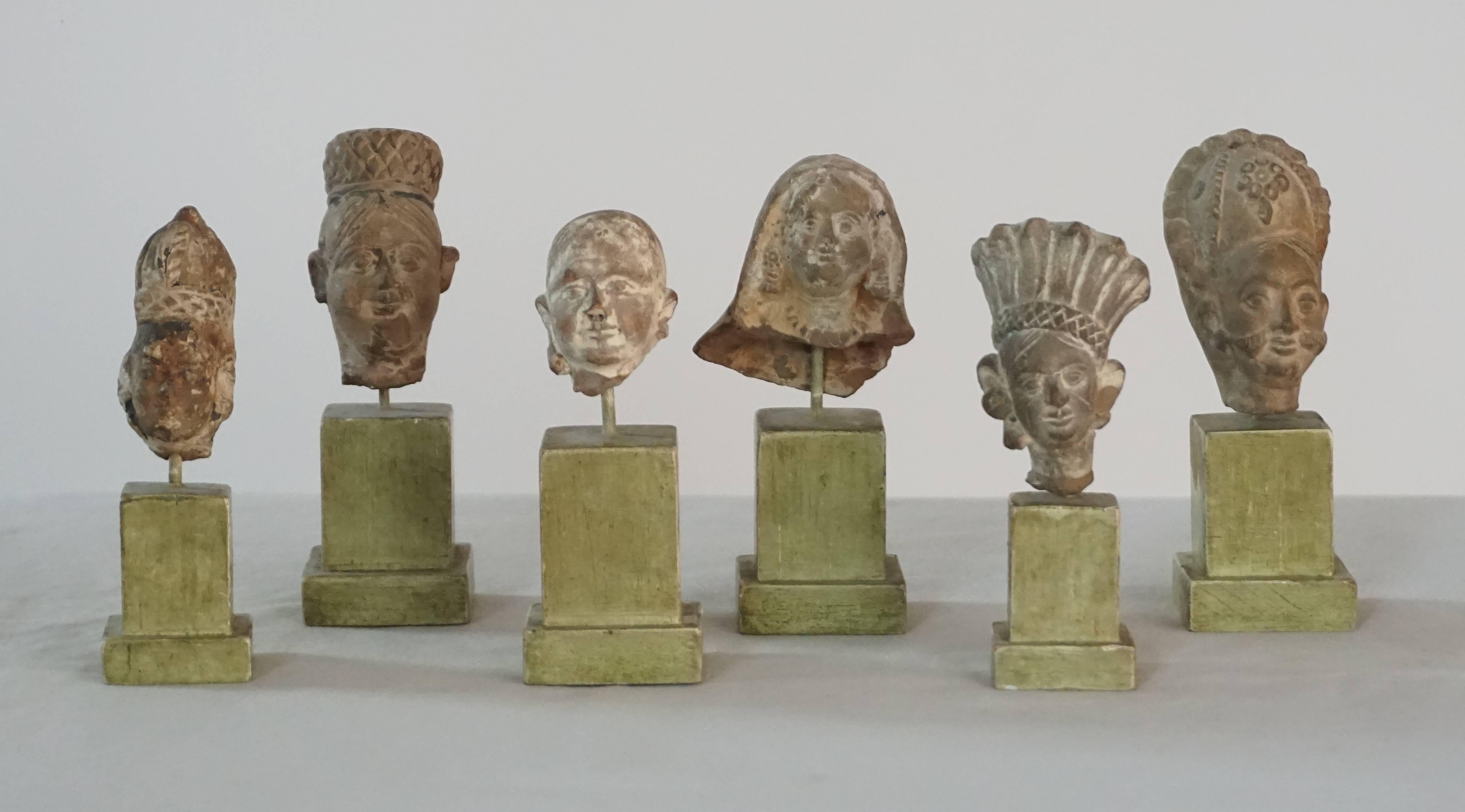 Collection of six ancient Indian Gandharan period (circa 1500 BCE - 535 BCE) terra cotta Greco-Buddhist miniature figurative busts of personages or deities mounted on contemporary painted column-form wood museum stands.  Largest measurements given