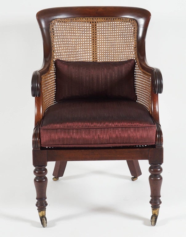 An elegant English William IV period mahogany caned armchair in the Regency taste having shaped crest rail above continuous caned back and sides with carved lotus-capped scrolled arm terminals above caned seat with squab cushion on baluster turned