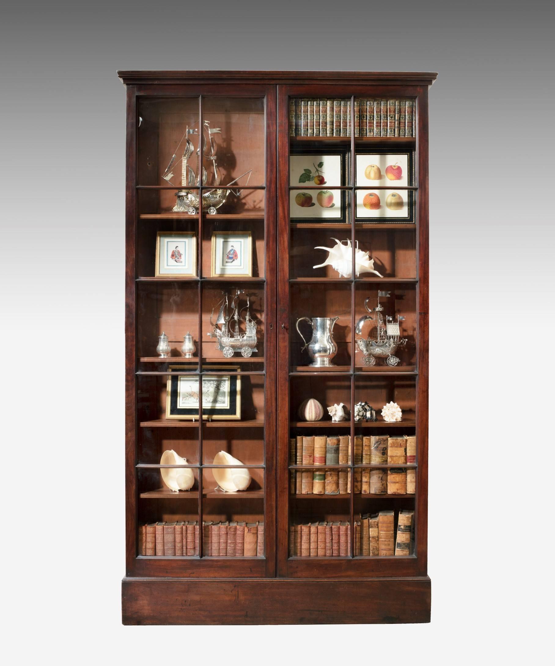 A George II period mahogany two-door bookcase; the stepped cornice above a pair of glazed doors which open to reveal adjustable shelves and raised on a plinth base. Retaining an excellent color and patination.

This bookcase's simple clean design