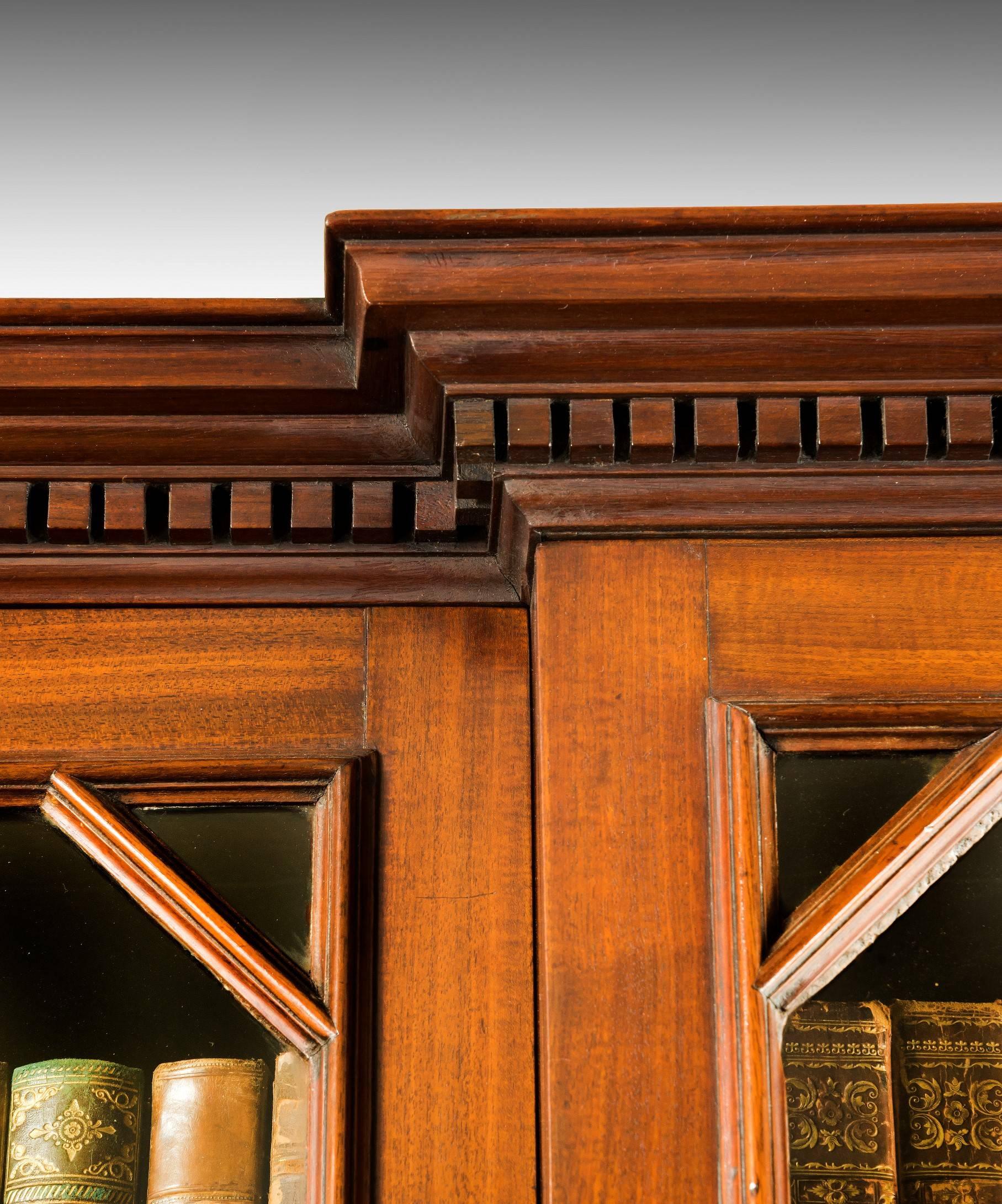 A handsome George II period mahogany breakfront bookcase; the bookcase's dentil moulded cornice above a central astragal glazed door flanked by a glazed door to either side which enclose fully adjustable bookshelves; below are a central bank of four