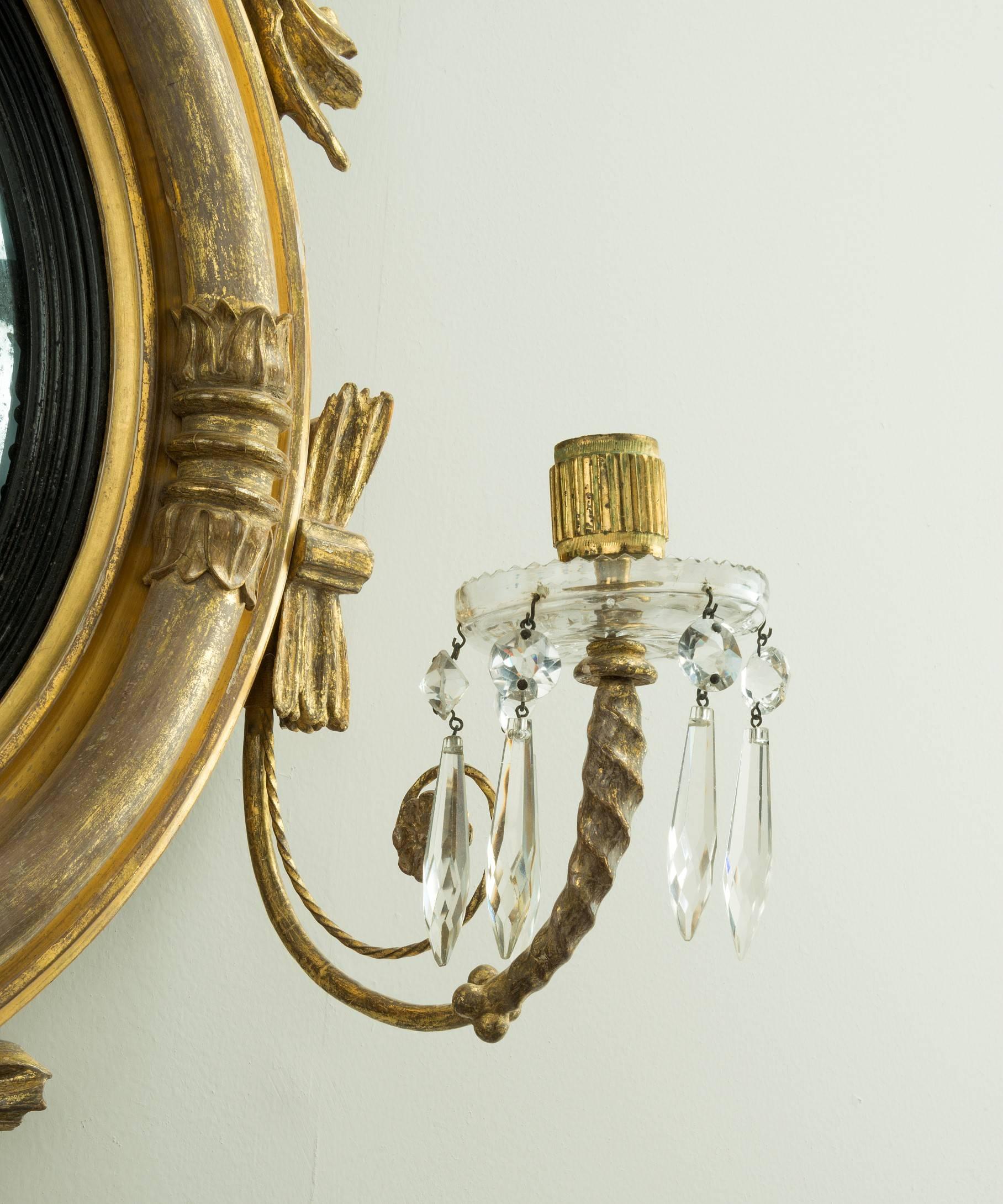 A Regency period carved giltwood convex mirror; the original convex mirror plate set within a reeded ebonized slip and a carved giltwood frame which is decorated with lotus leaves; the mirror frame is surmounted by an eagle flanked by snakes