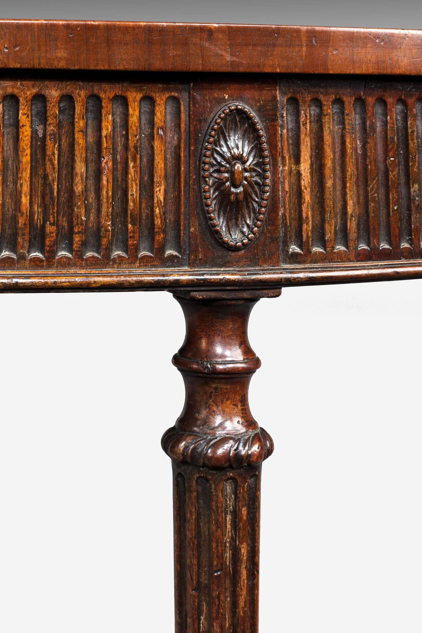 An elegant George III Adam period mahogany demilune console table; the console table's well figured fiddle back mahogany top above a fluted frieze centred by an entablature decorated with a crisply carved neoclassical urn and raised on elegant