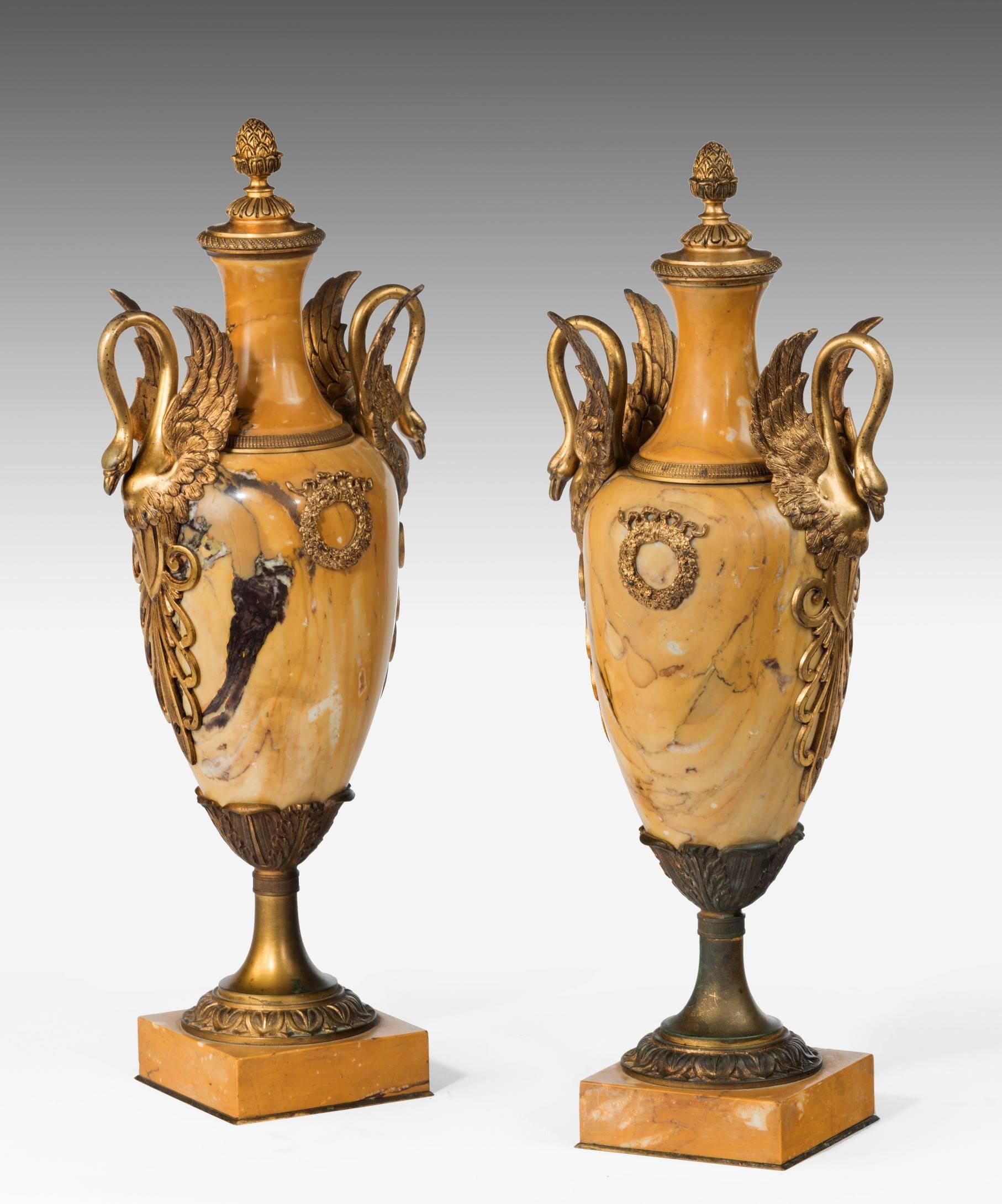 An elegant pair of late 19th century marble and ormolu vases; the vase's siena marble body mounted in ormolu with an acorn finial and scrolling swans to either side of the body and a laurel wreath to the centre of the body; the vase raised on a