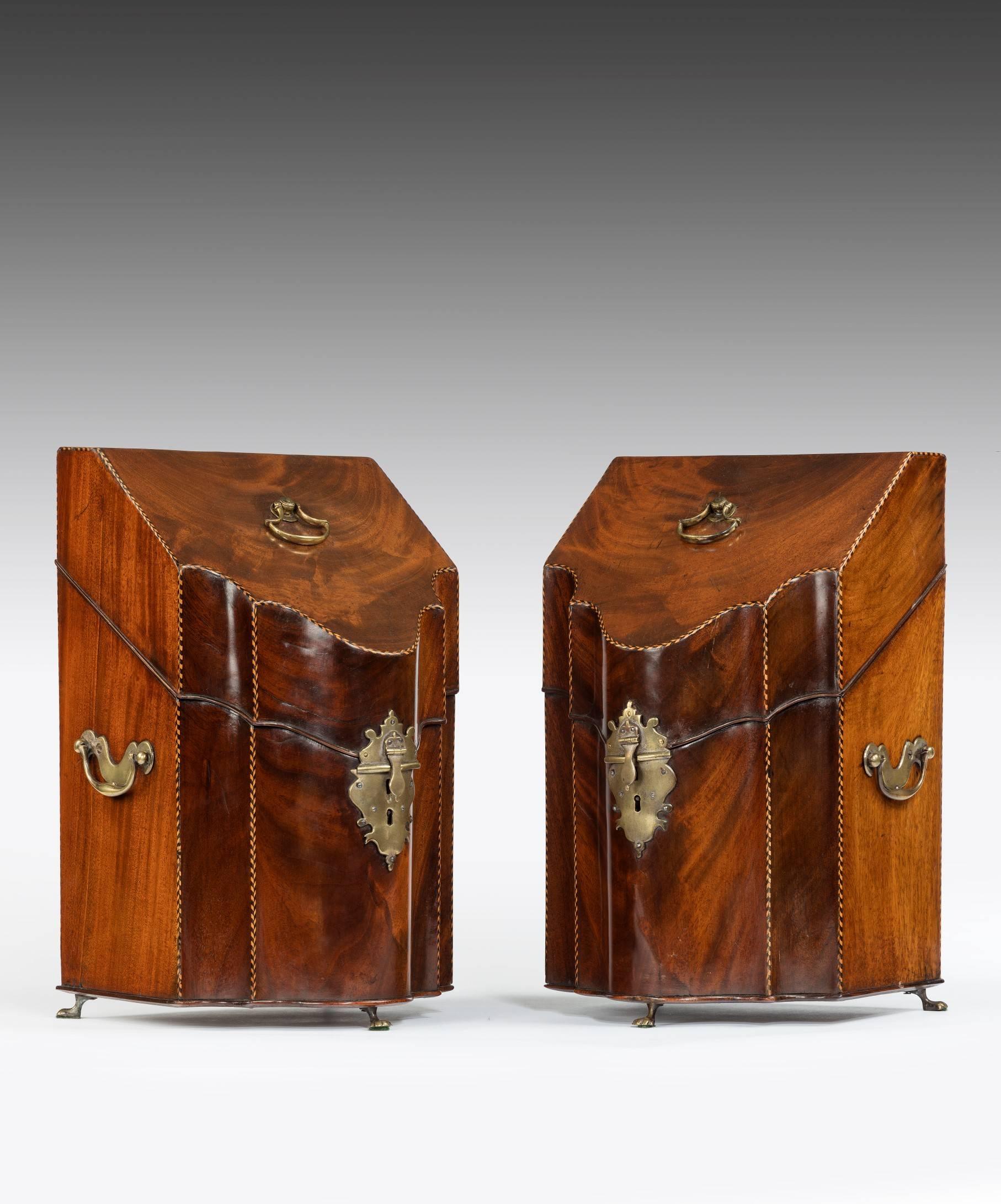 A pair of George III Sheraton period mahogany knife boxes; the knife box's lift-up lid is veneered in flame Cuban mahogany with barber's pole stringing and retains the original axe-head handle, the lid opens to reveal a fully fitted interior. The