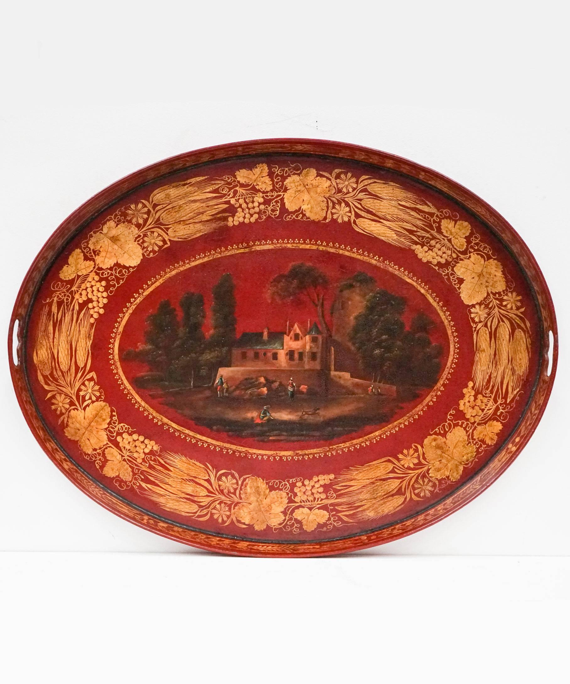 An extremely decorative French, 19th century scarlet toleware tray on a bespoke stand; the toleware tray painted in scarlet red and decorated in gilt with a bold border of vine leaves and wheat ears encircling a village scene raised on a