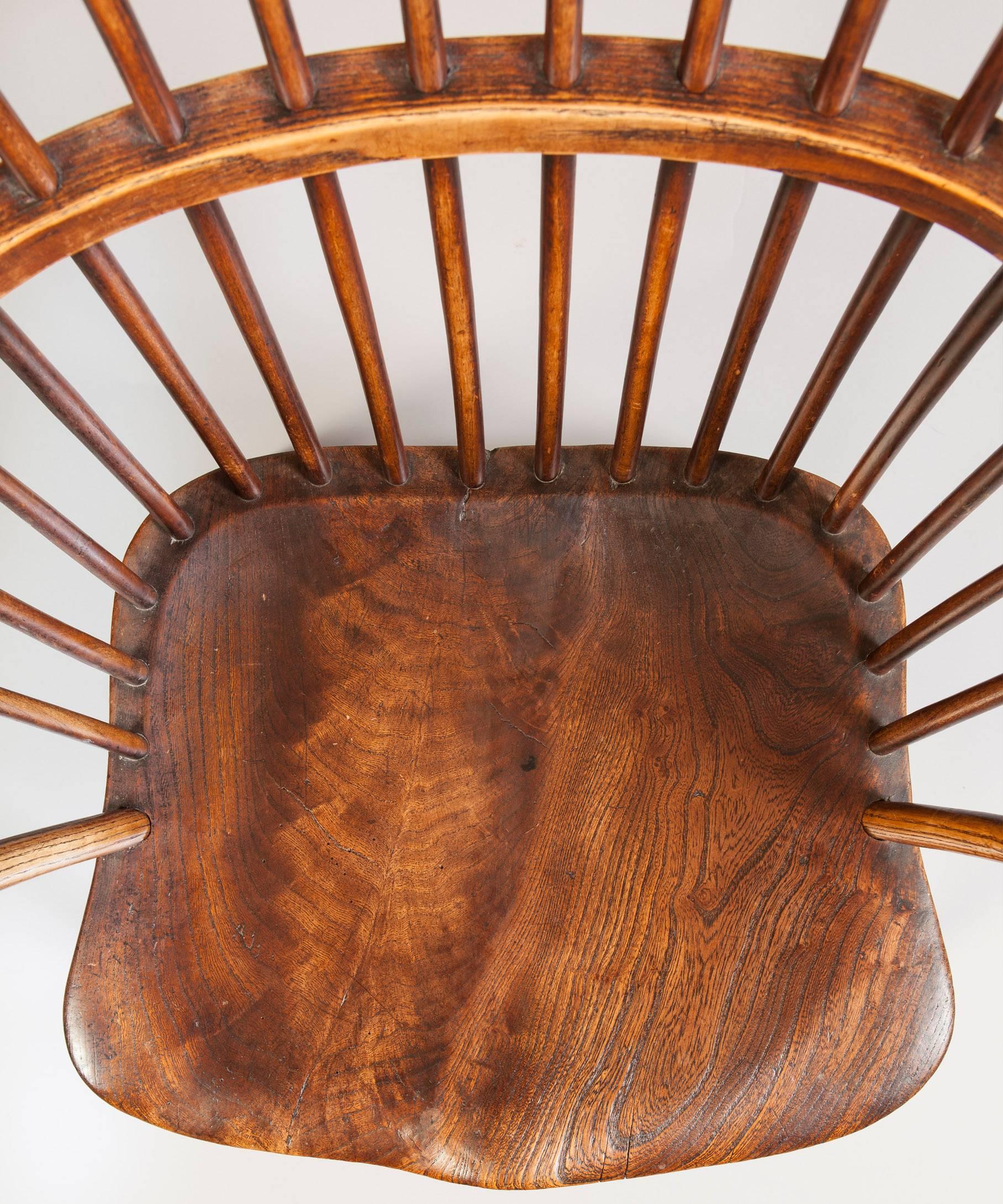 An early 19th century comb back armchair in the Welsh vernacular tradition; the armchair's curved fruitwood top rail above turned fruitwood spindles and ash arms; the armchair's comfortable seat is shaped from a beautifully figured piece of elm and