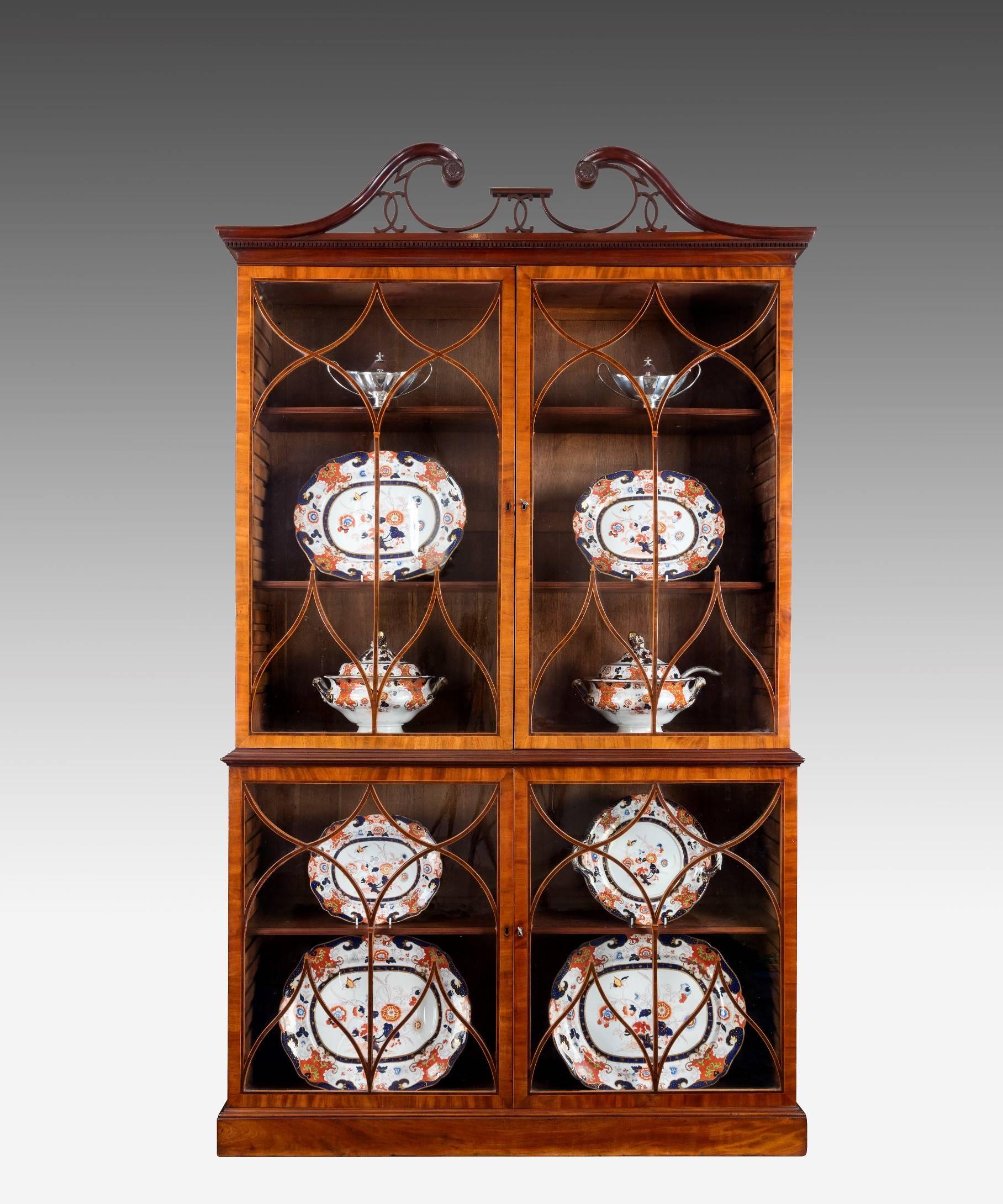 A George III period Hepplewhite mahogany china display cabinet or bookcase, the elegant swan neck pediment above Gothic astragal glazed doors to the top and base which are cross banded in mahogany and tulipwood and strung in boxwood and open to