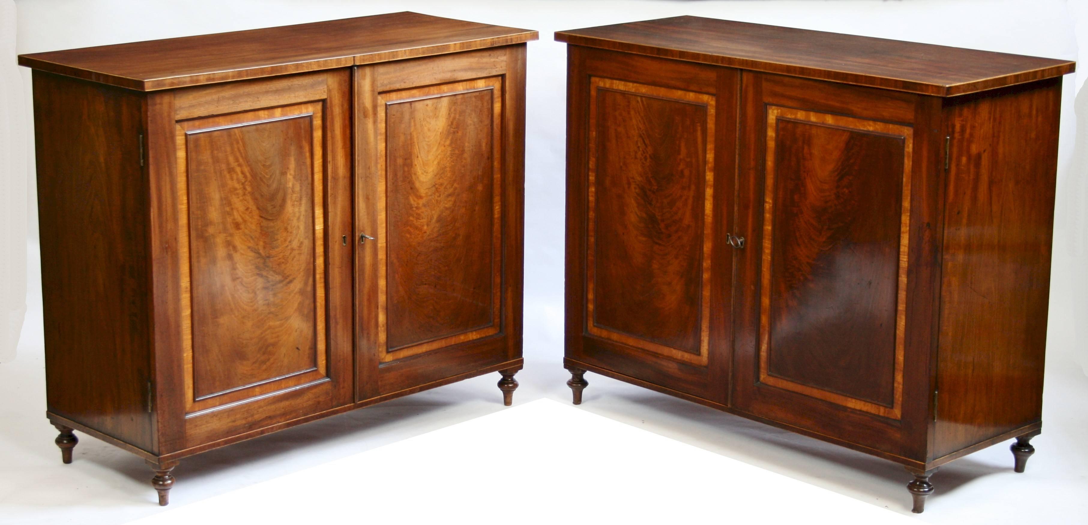A fine pair of Georgian cabinets by Gillows of Lancaster; the cabinet doors veneered with well figured Cuban flame mahogany and crossbanded in satinwood opening to reveal drawers with fire gilded brass swan neck handles; raised on turned