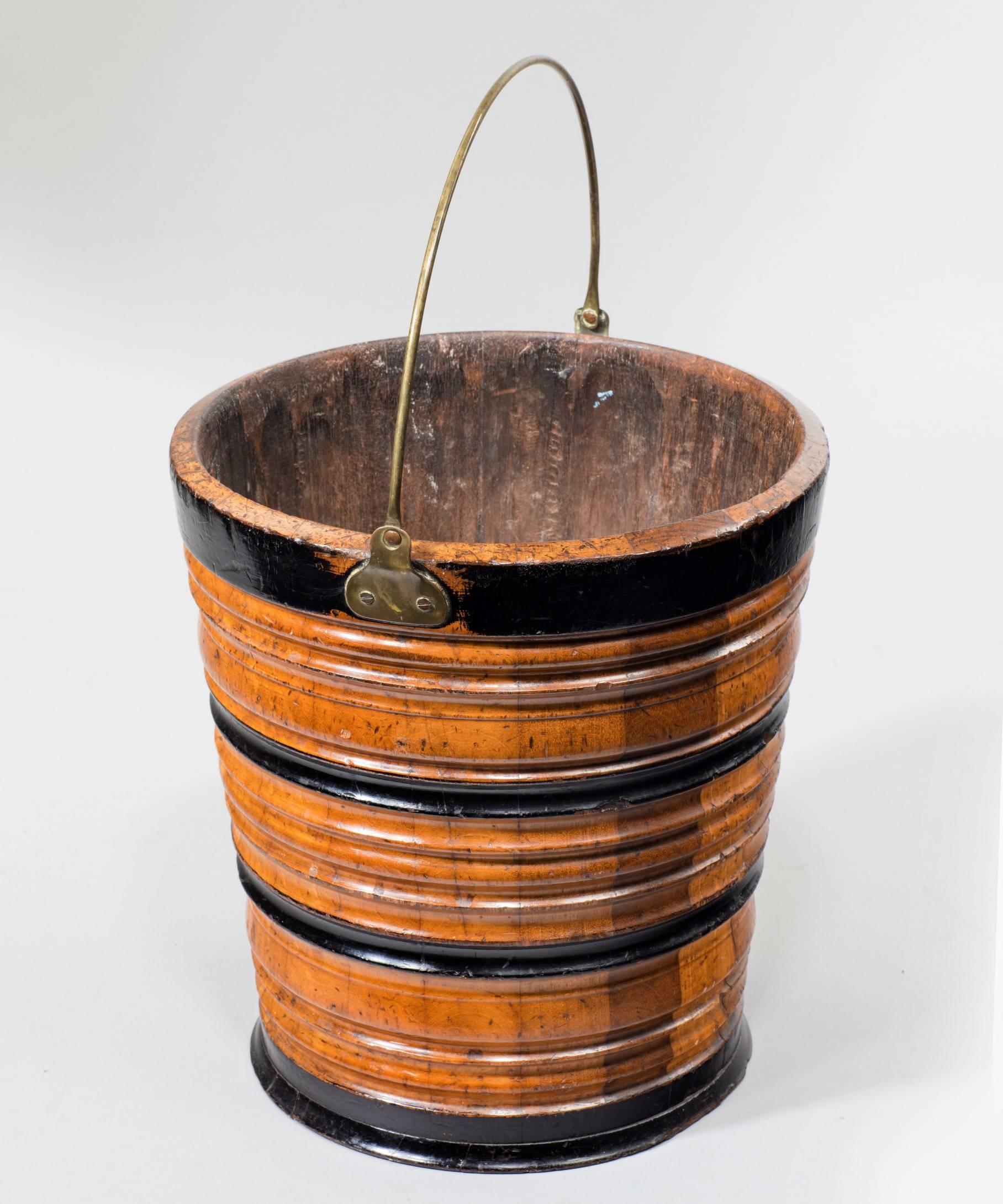 A 19th century Dutch bucket in fruitwood and ebonised wood of coopered construction with a ribbed body and a brass carrying handle. This bucket is often referred to as a 'Teestoof' which was used for keeping a kettle warm over a bed of smouldering