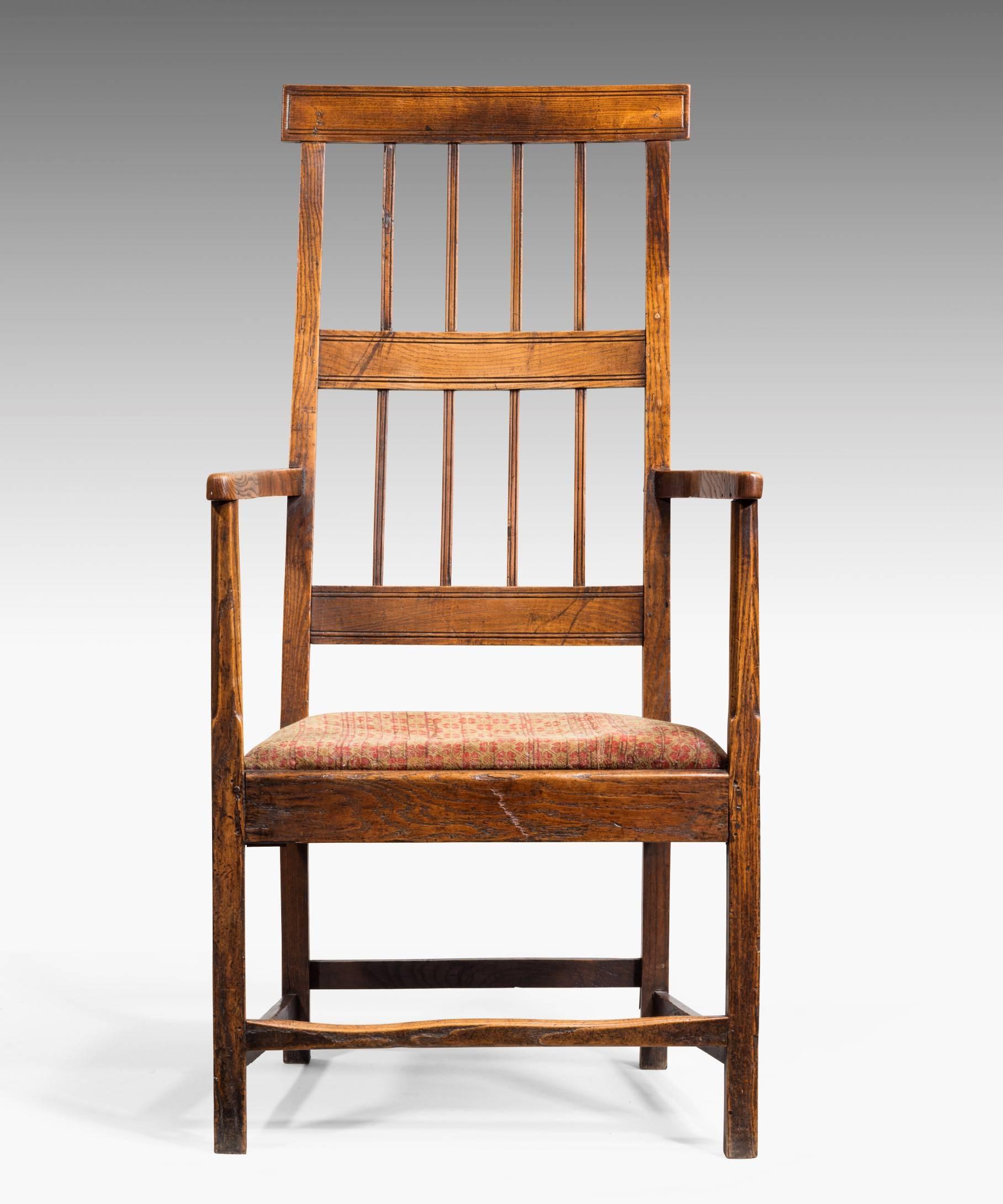 An elegant Georgian elm armchair in the country tradition; the unusually high bar back with a tablet top rail above outswept arms and an upholstered seat raised on square legs united by beautifully worn stretchers. This armchair has an unusually