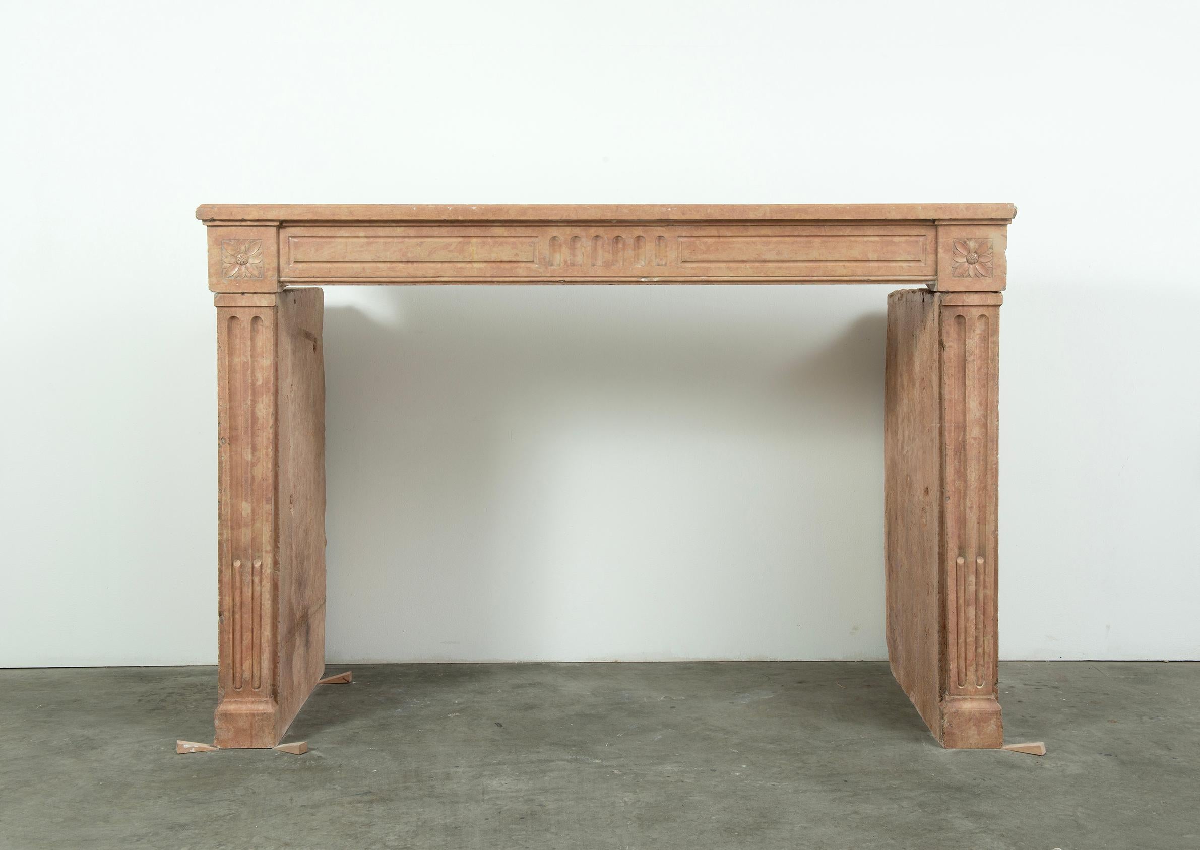 This elegant French Louis XVI mantel is carved from soft-toned limestone, epitomizing the restrained neoclassical style of the late 18th century. Its clean, rectilinear profile – with a broad rectangular shelf and straight, fluted jambs – echoes the