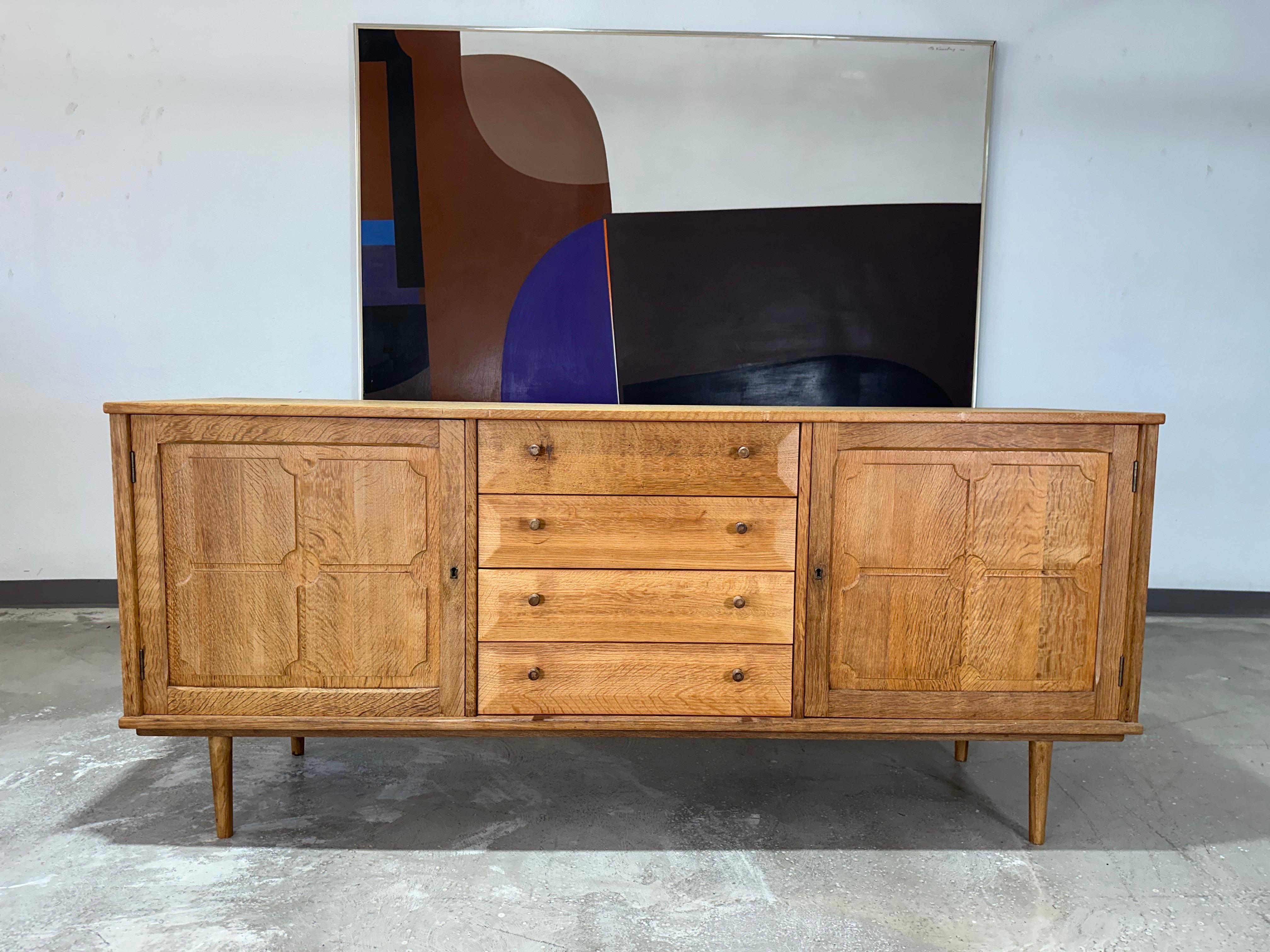 Vintage Danish solid oak brutalist sideboard credenza c1970’s attributed to Henning Kjaernulf. Carved panels on locking doors at left and right open to one felt lined drawer and one shelf in each side. Center features four bevel edge drawers with