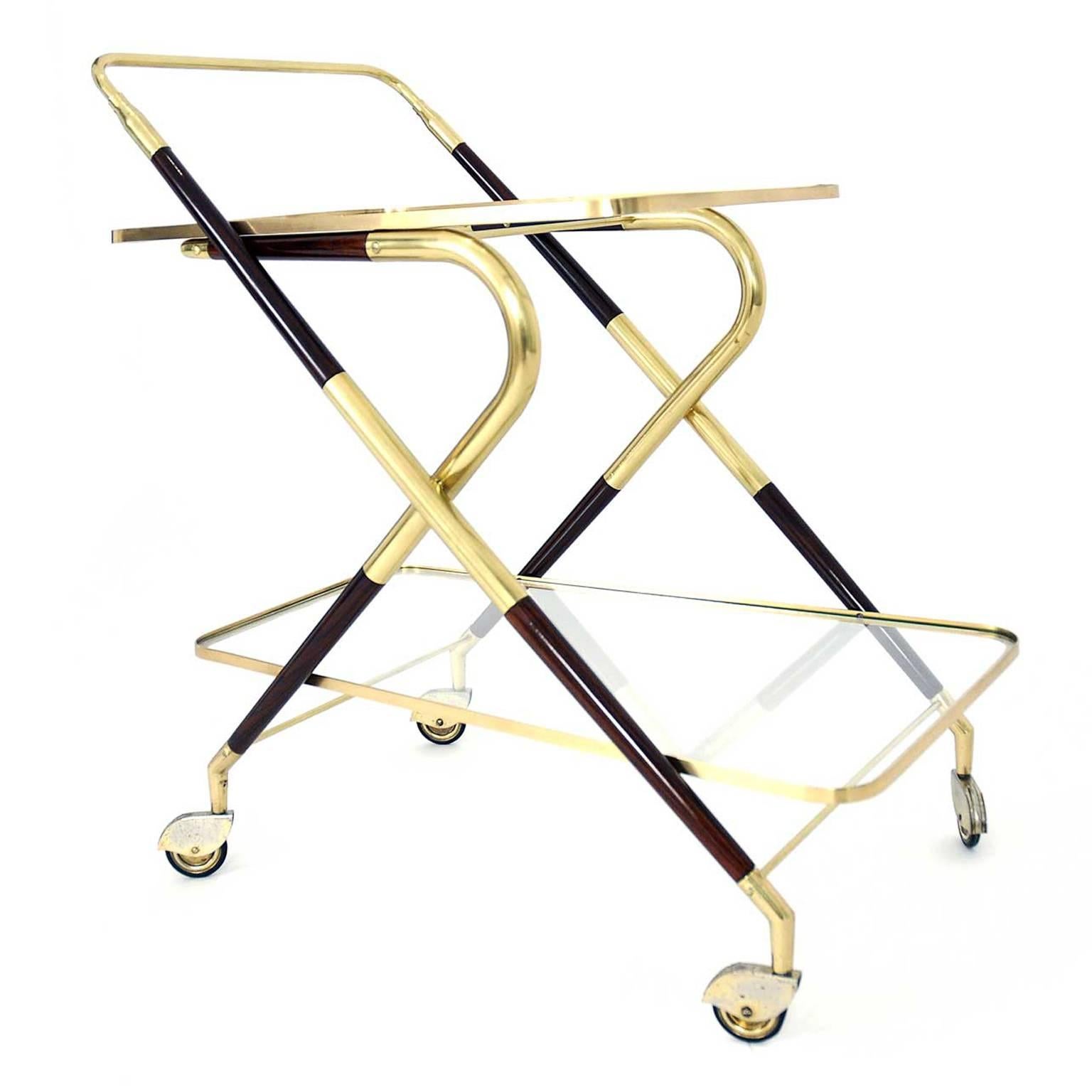 The frame of the serving cart is made of brass and wood, which is stained in mahogany. The wheels are also made of brass. The piece was designed in 1950 in Italy.