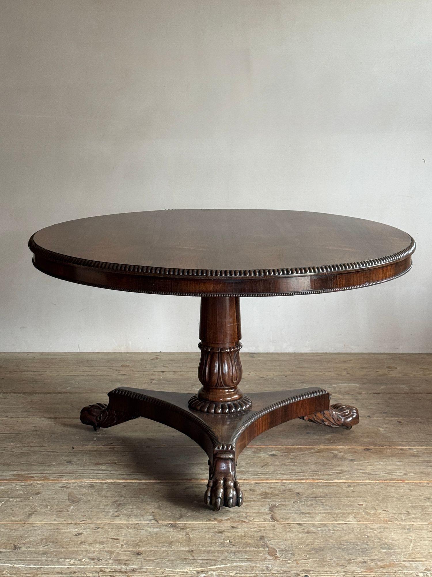 A smart early 19thC rosewood breakfast table, the tilt top with quarter beaded edge, above a carved baluster pedestal with gadrooned base on a triform plinth with finely carved lions paw feet with castors. In the manner of Gillows C.1830 Dimensions: