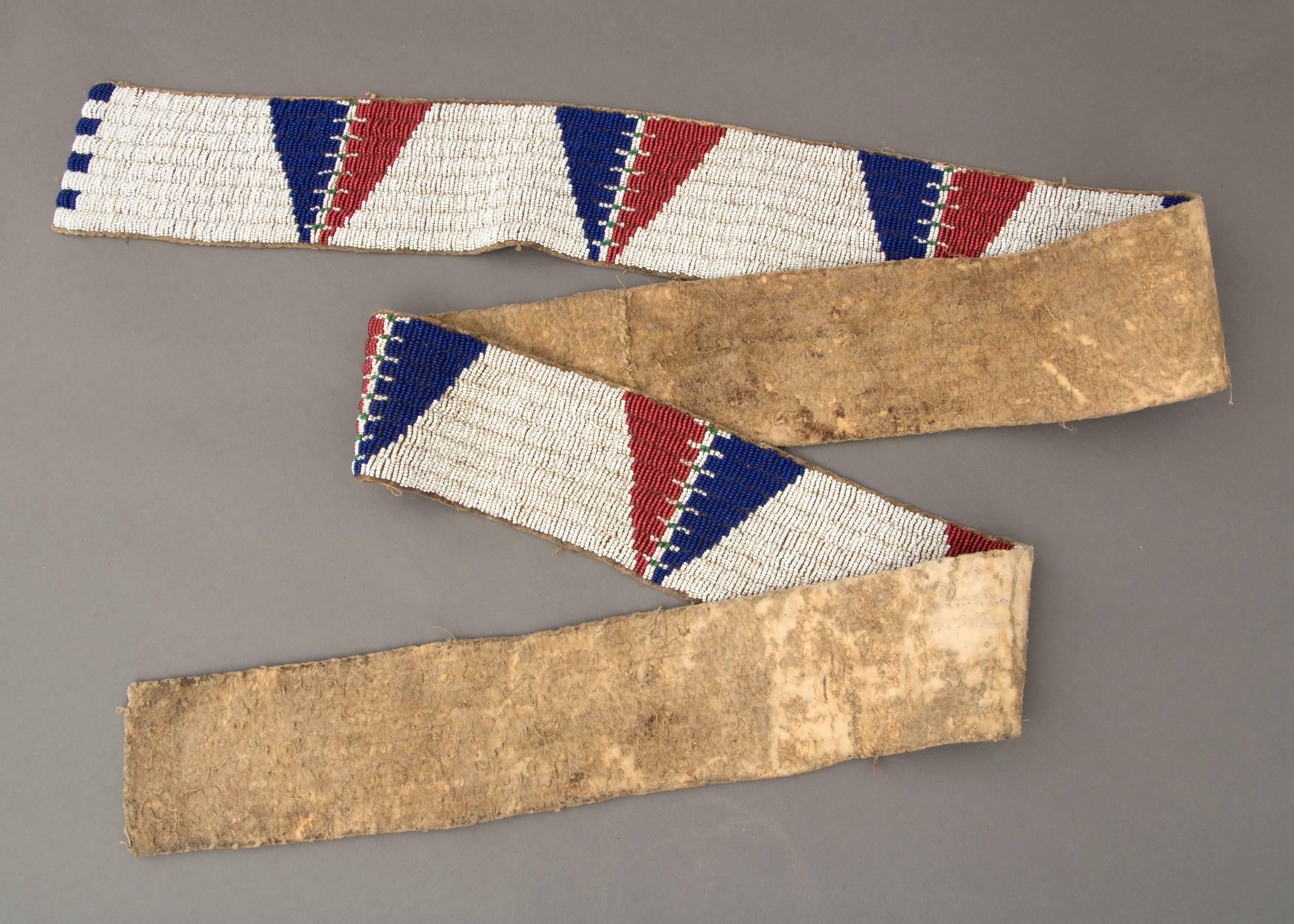 Originally created as two beaded strips which adorned a pair of leggings, these were later joined together, possibly for reuse as a blanket strip. Constructed of native-tanned hide and beaded with stylized tepee (tipi) motifs in red and blue against