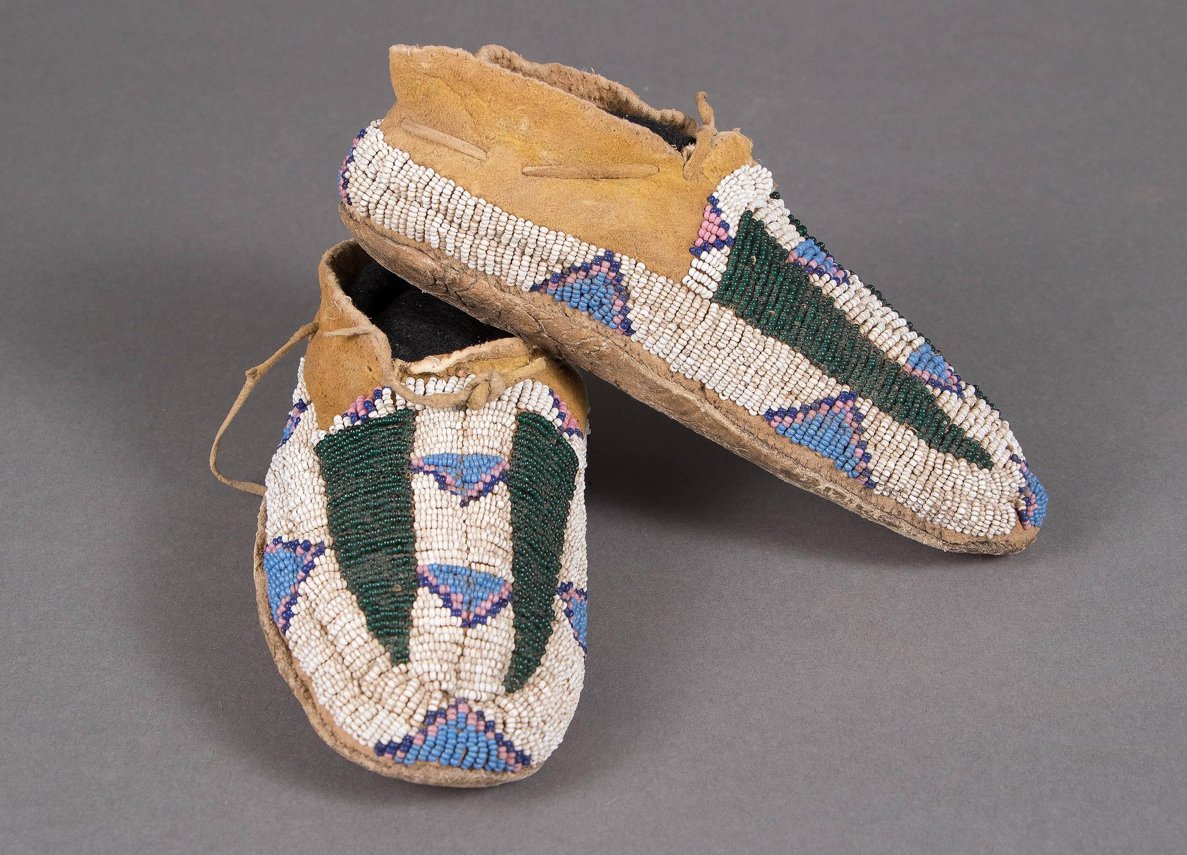 A youth or child's pair of moccasins. Constructed of native tanned hide and intricately beaded with glass trade beads with green 