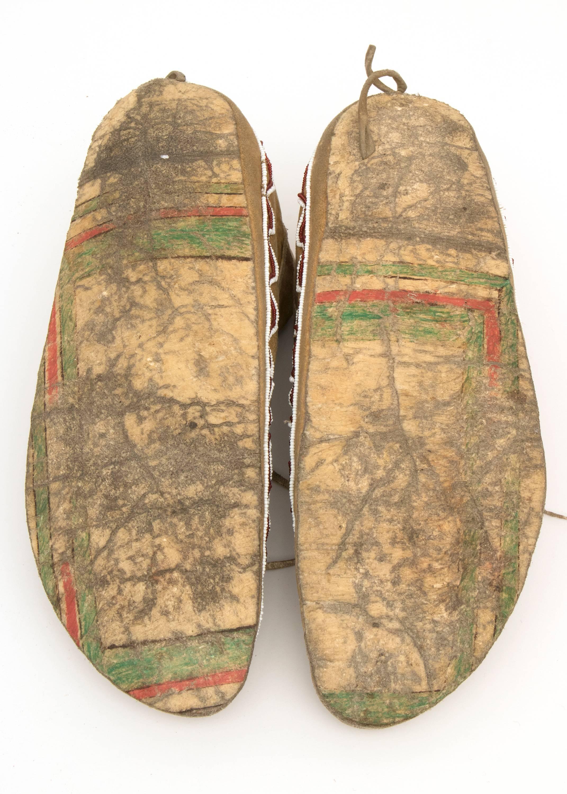 Constructed of native tanned hide and artfully beaded with blue, white and red trade beads; the maker recycled portions of painted parfleche for the soles. Each moccasin measures 10.75 x 3.75 x 4.75 inches. 

The Kiowa, a nomadic tribe of the