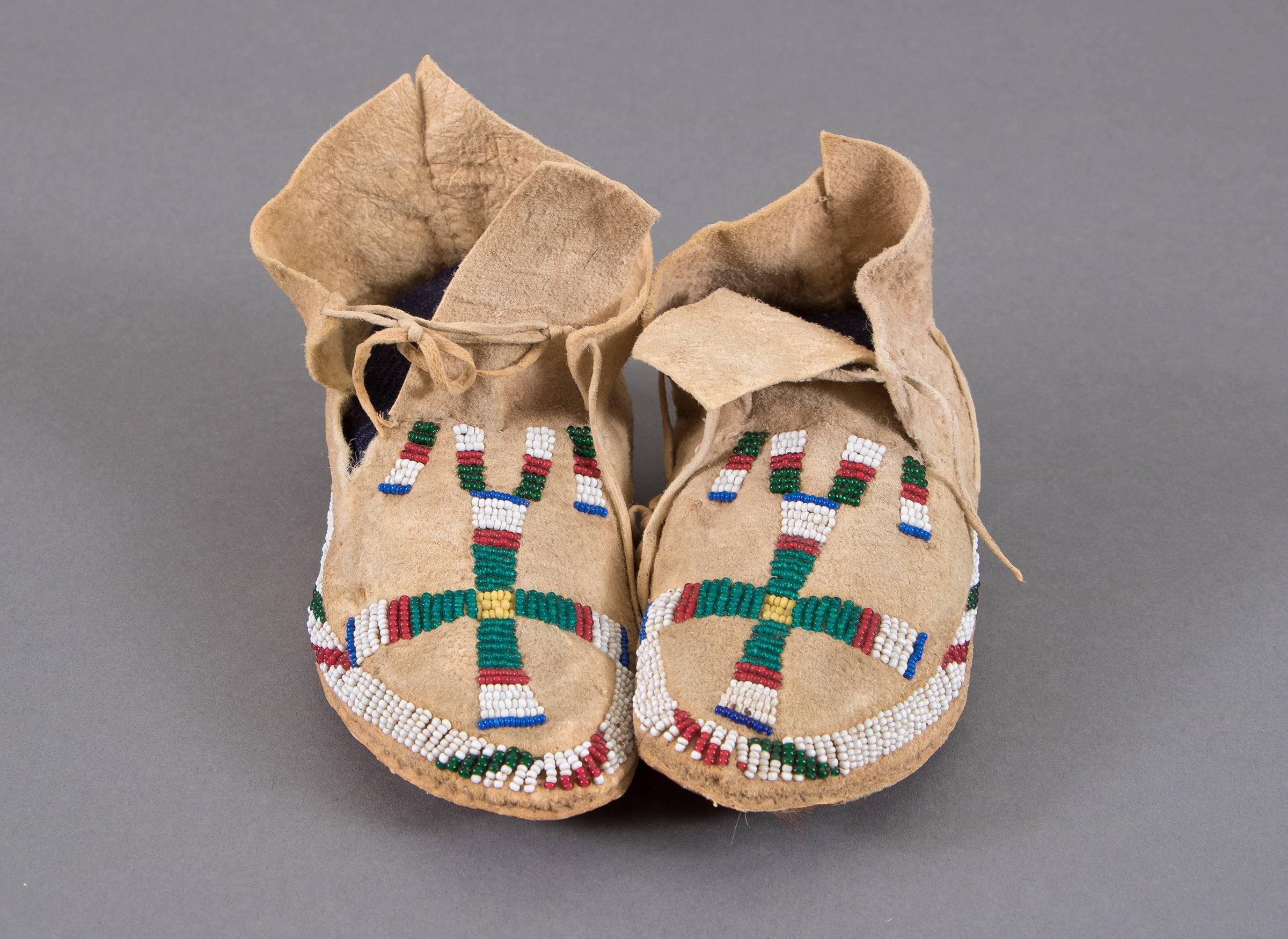 A remarkable pair of child or youth-sized moccasins created between 1875-1900. Constructed of native tanned hide and partially beaded in red, yellow, green, white and blue trade beads. A stylized cross adorns each vamp. 

The Cheyenne migrated with