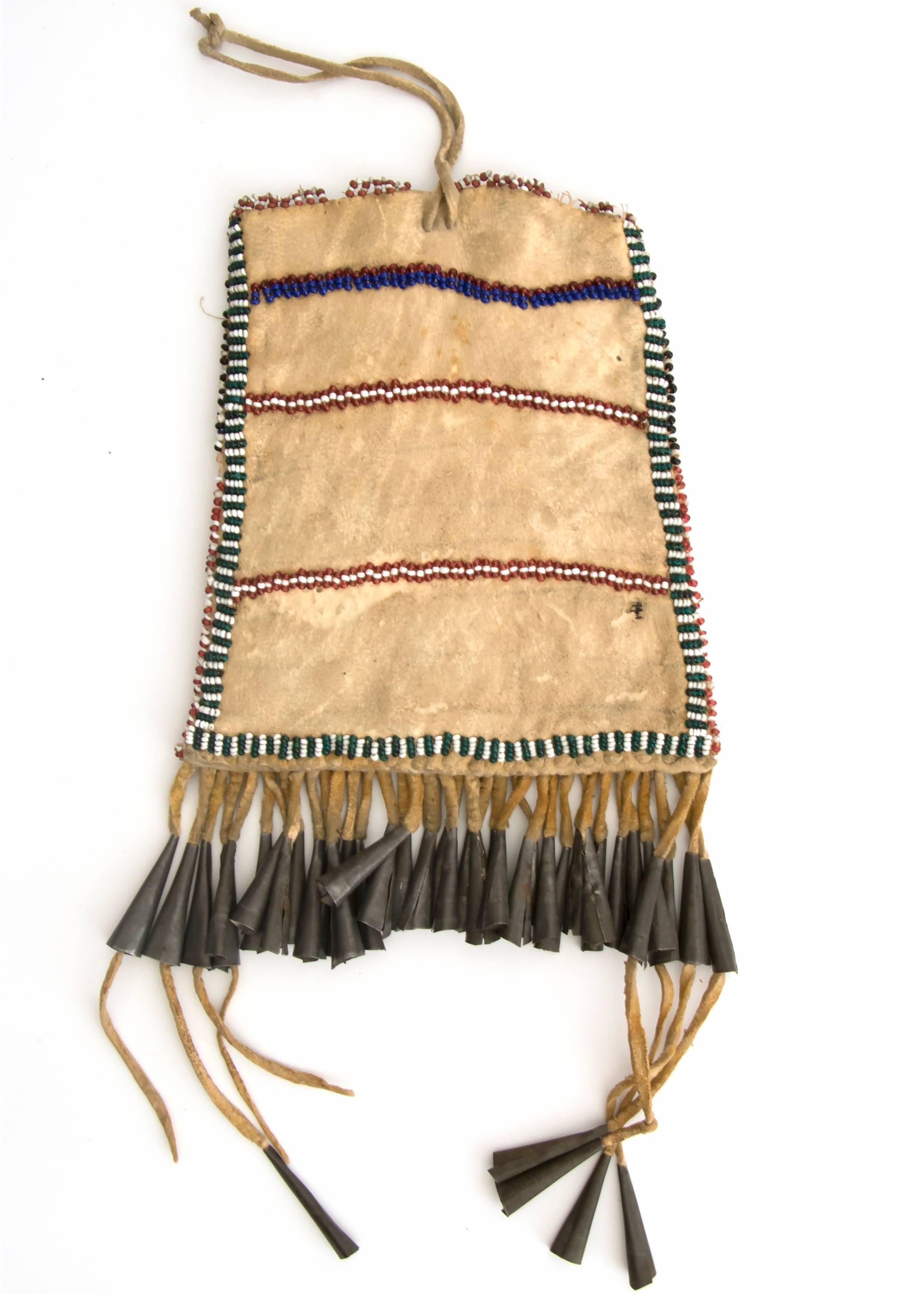 A Strike-A-Light pouch constructed of Native tanned hide with glass trade beads in red, white, green, yellow, black and blue. Fringed with and tin cone tinklers and a brass button.

A nomadic tribe, the Apache peoples originated in Alaska and