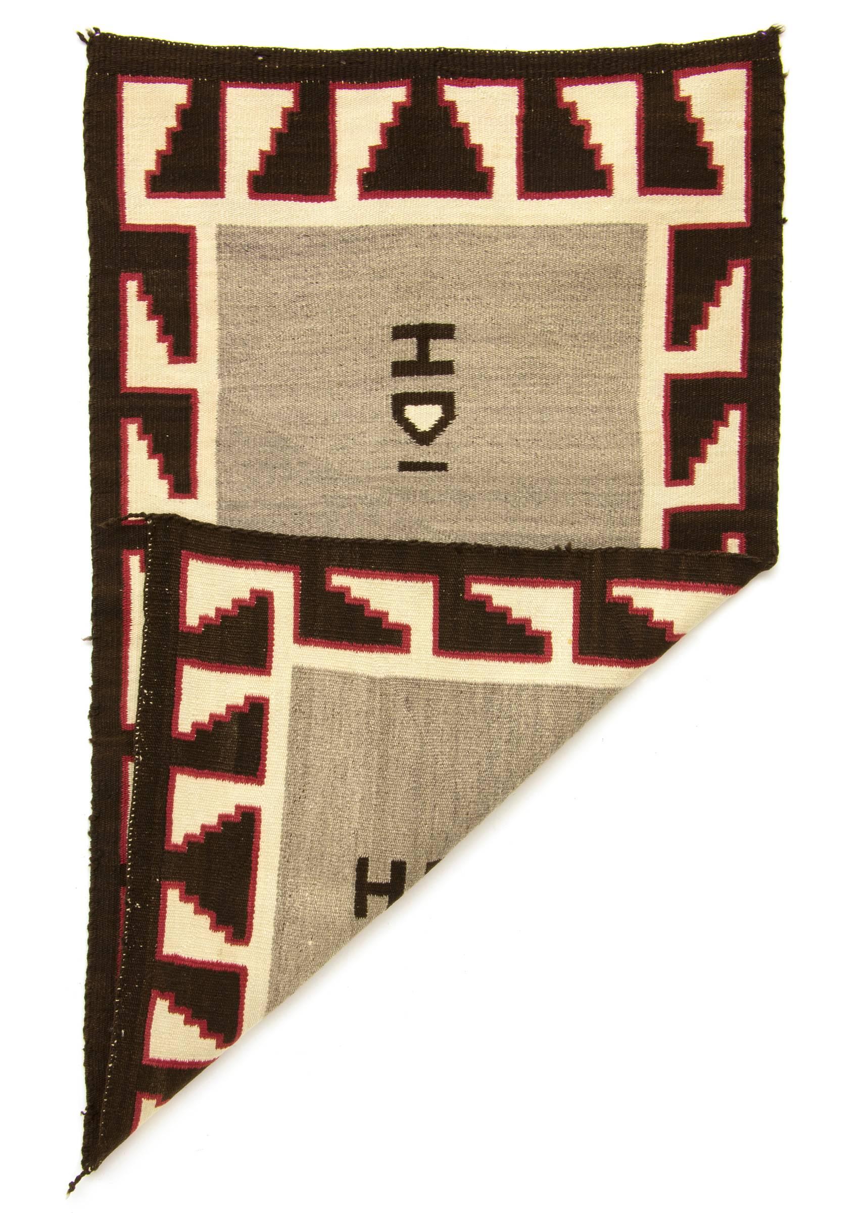 A double saddle blanket woven of native hand-spun wool in natural fleece colors of gray, ivory and brown/black with aniline dyed red. A geometric stepped border surrounds a gray field.