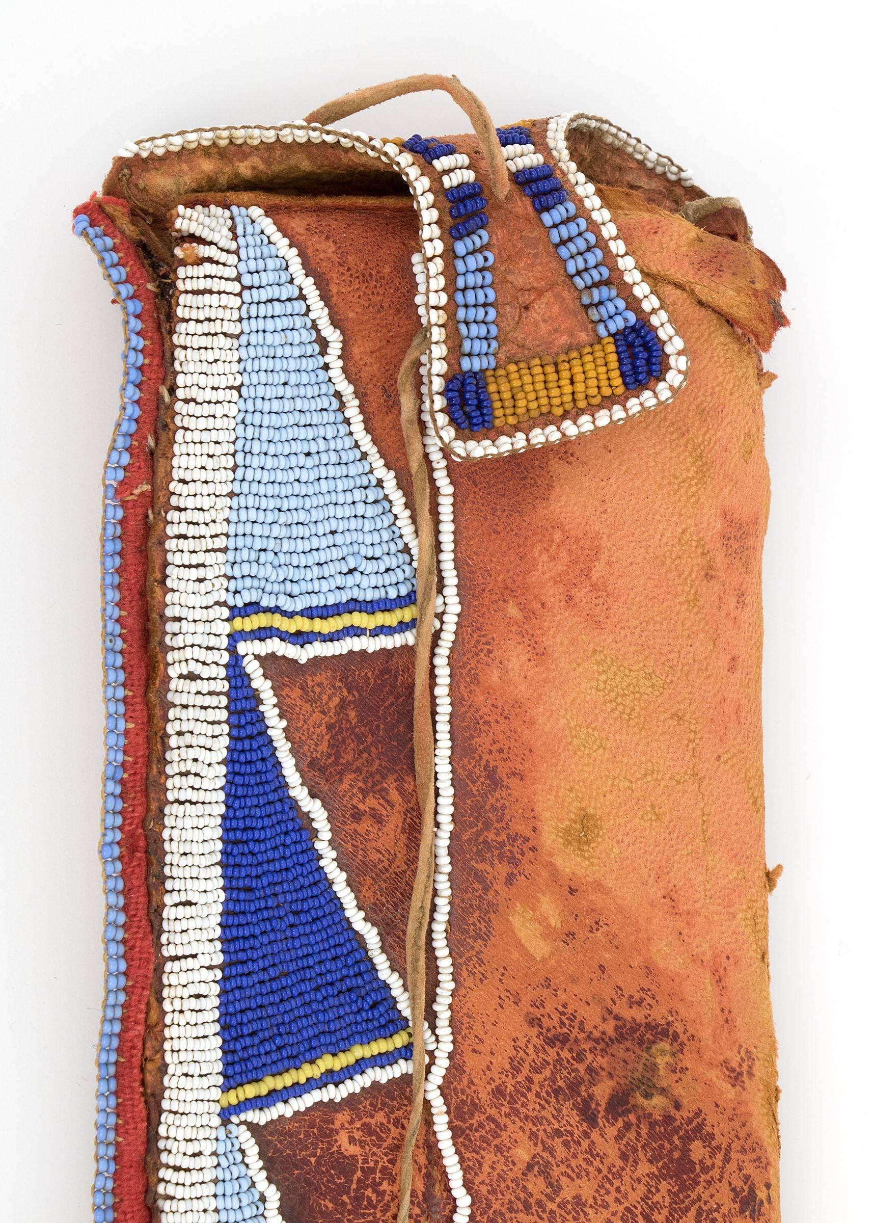 A Classic Period (Pre-Reservation era) knife sheath created circa 1870 by a Crow (Plains Indian/Native American) artist.  Constructed of Native tanned hide and partially beaded with blue, white and yellow trade beads.  There is red trade cloth along