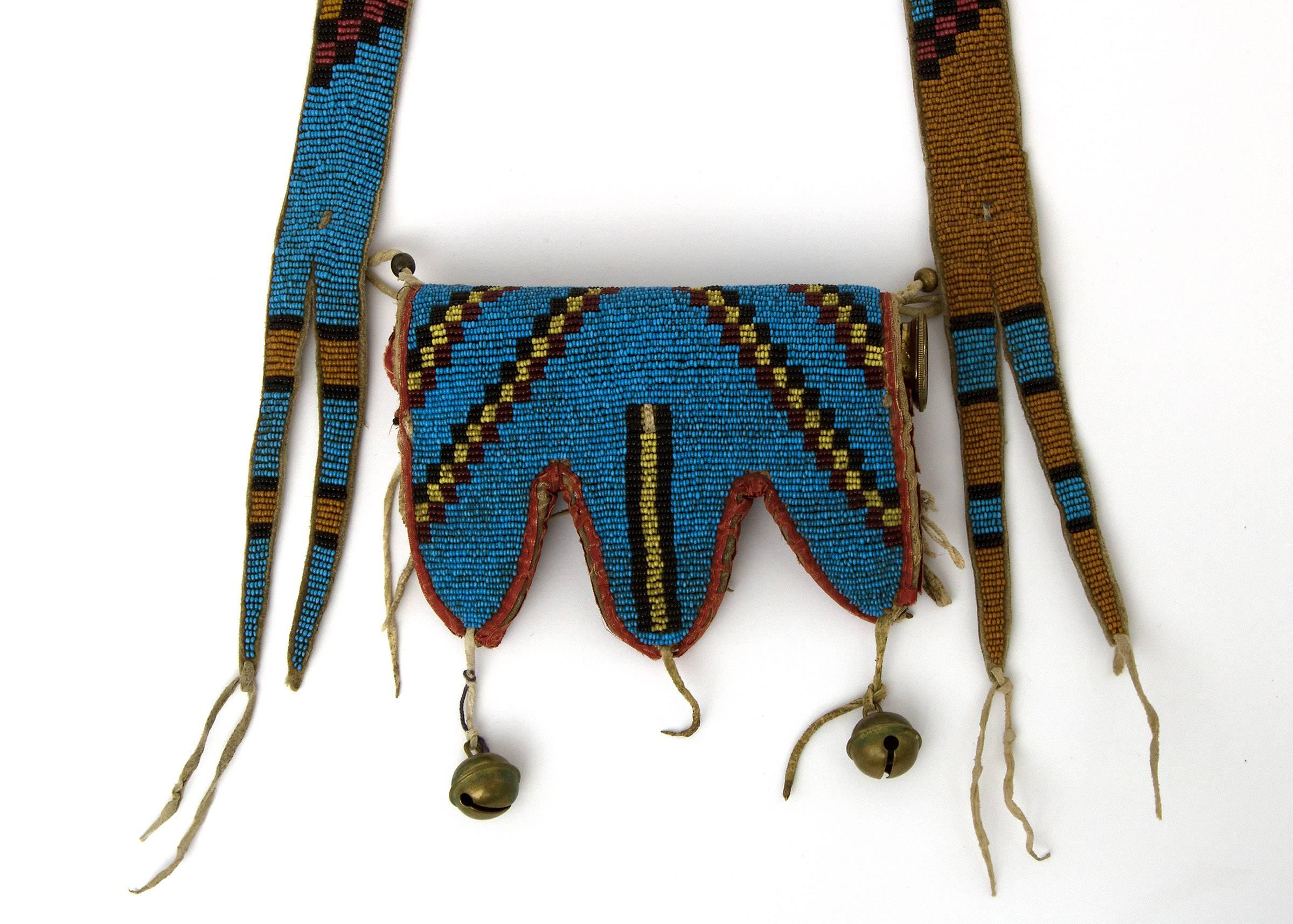 A 19th century American Indian beaded telescope case (Blackfoot/Blackfeet). The case is composed of native tanned hide and beaded in red, yellow, pumpkin and black trade beads in geometric motifs against a blue field. Bottom is edged in cotton cloth