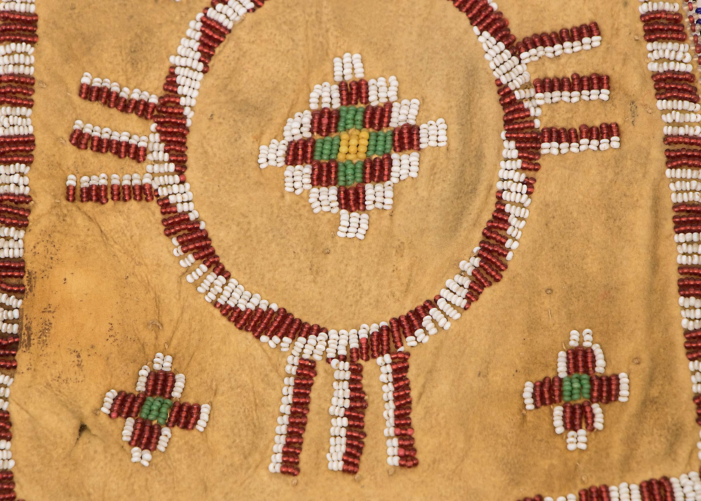 Constructed of native-tanned hide and partially beaded with cross and geometric devices. Beadwork fringe at the bottom.
The Apache, a nomadic American Plains Indian tribe, followed the buffalo and ranged across the American Southwest including areas