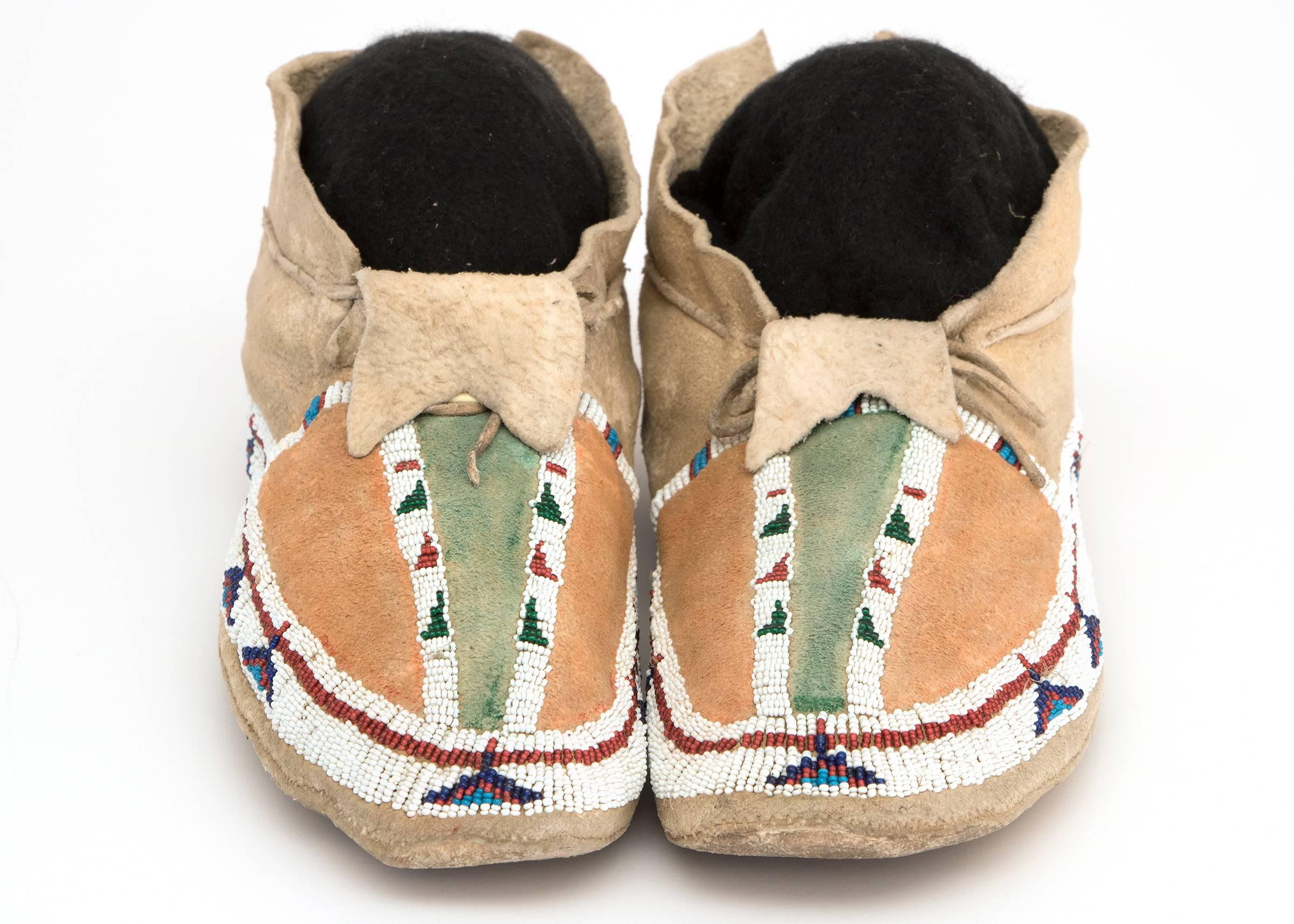 A pair of Southern Cheyenne (Plains Indian) Moccasins created circa 1890. Constructed of Native-Tanned hide and partially beaded with glass trade beads with stylized Tepee motifs. The beadwork surrounds two Buffalo Tracks along the vamps and the
