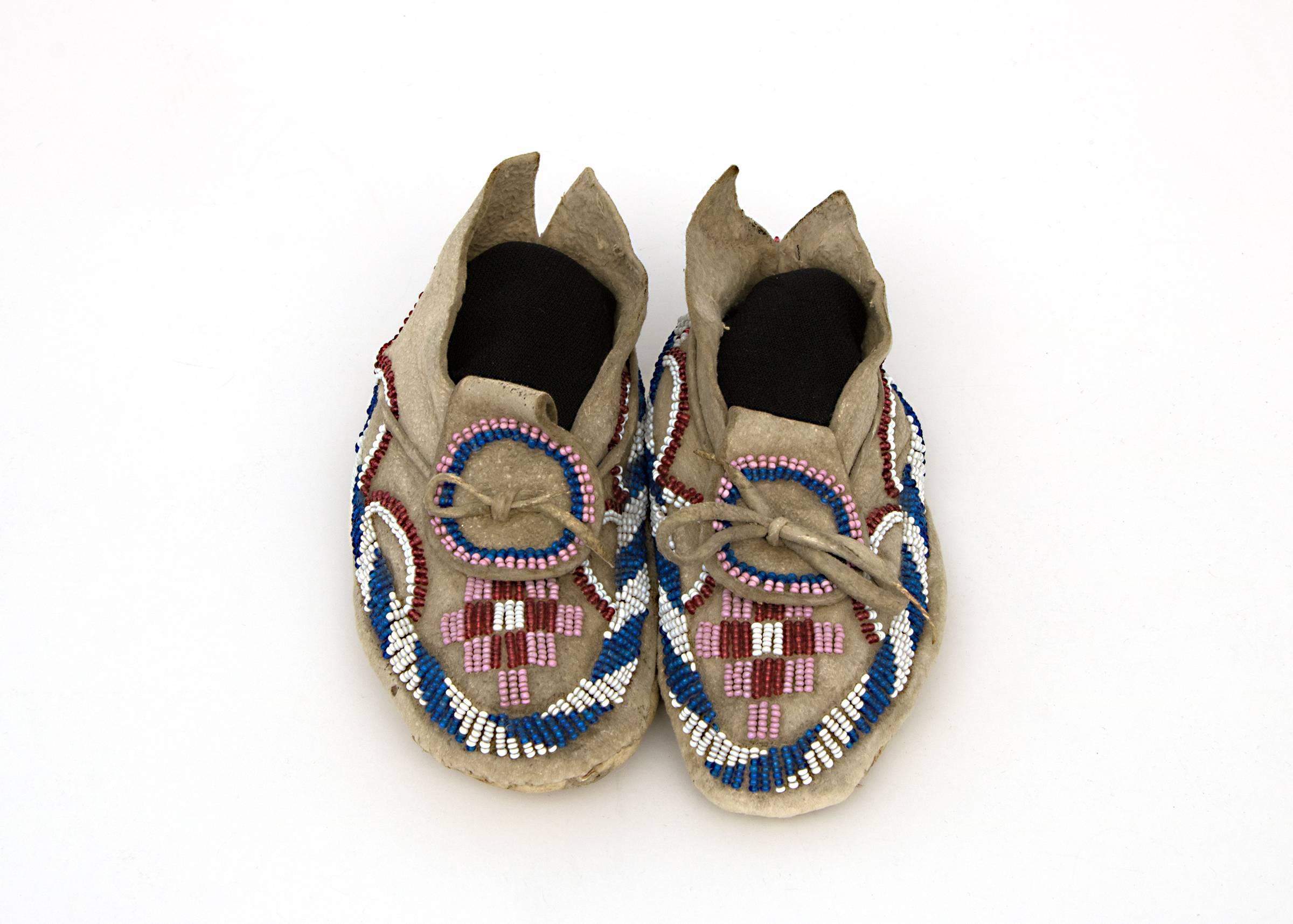 A pair of 19th century antique Native American child size beaded Kiowa-Apache (Plains Indian) moccasins. Constructed of Native tanned hide, sinew-sewn and partially beaded with trade beads in red, pink, white and blue, circa 1875-1900.  
The Kiowa,