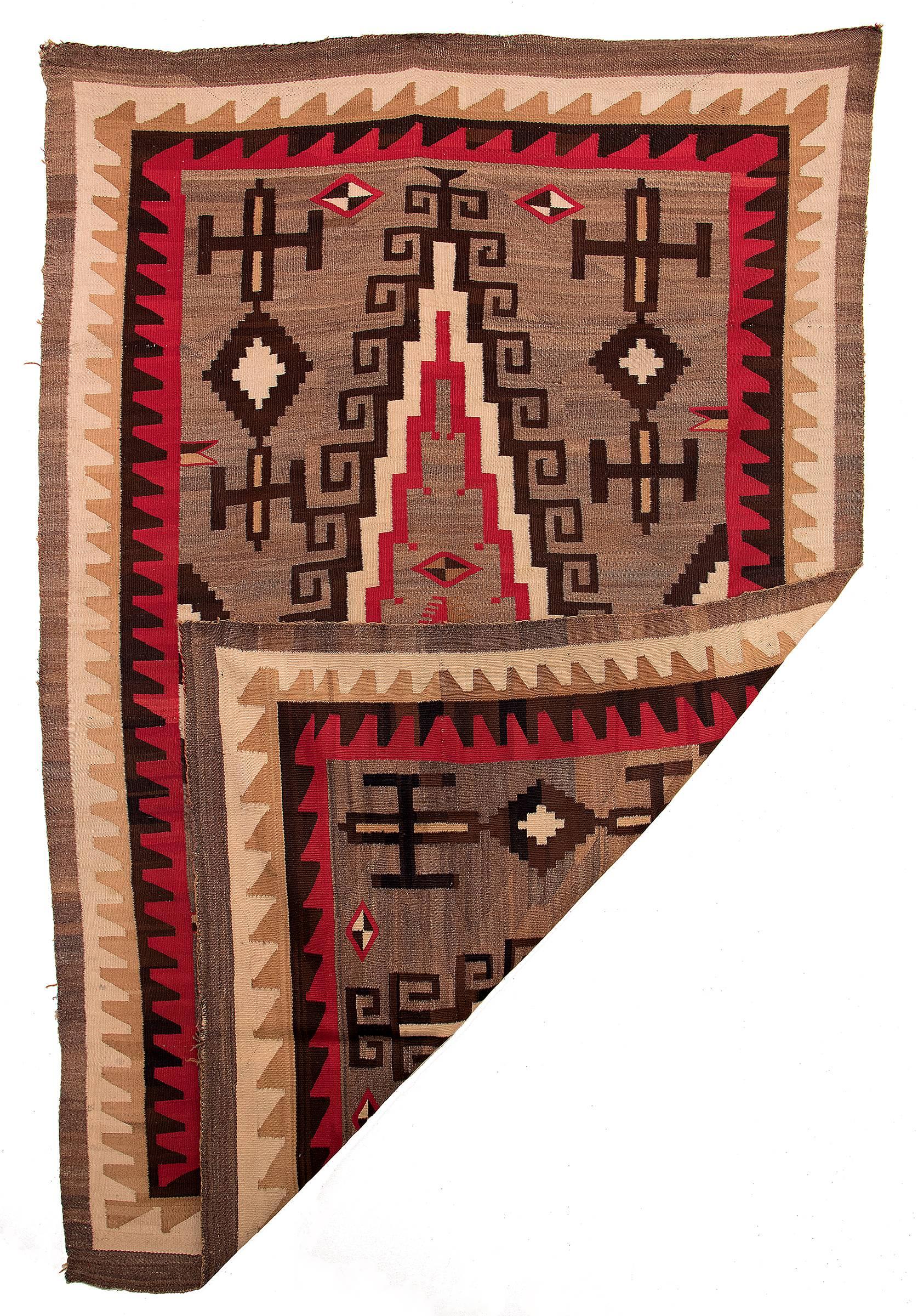 A regional rug, likely woven at Ganado (Hubbell Trading Post) in Arizona. This textile is woven of natural black, gray, ivory and camel/light brown fleece with aniline red.

This textile is well suited for use on the floor as an area rug, as a
