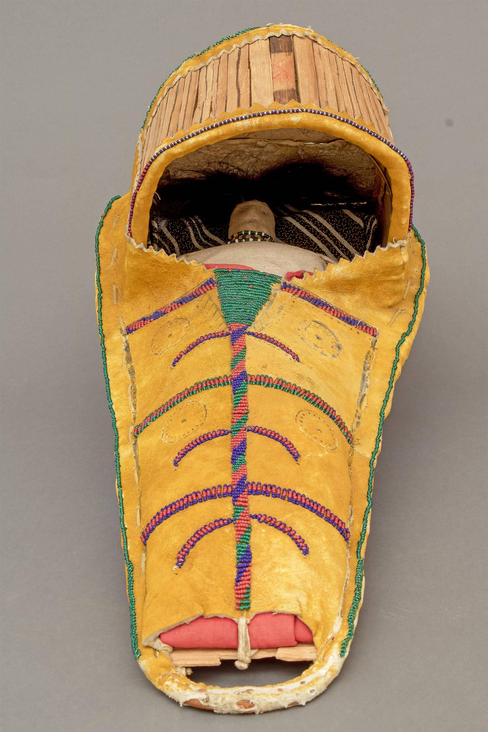American Indian girl's toy cradleboard with a doll laced inside. Constructed of native tanned hide stretched over a wooden frame and decorated with yellow ochre pigment and glass trade beads.

A nomadic tribe, the Apache peoples eventually settled