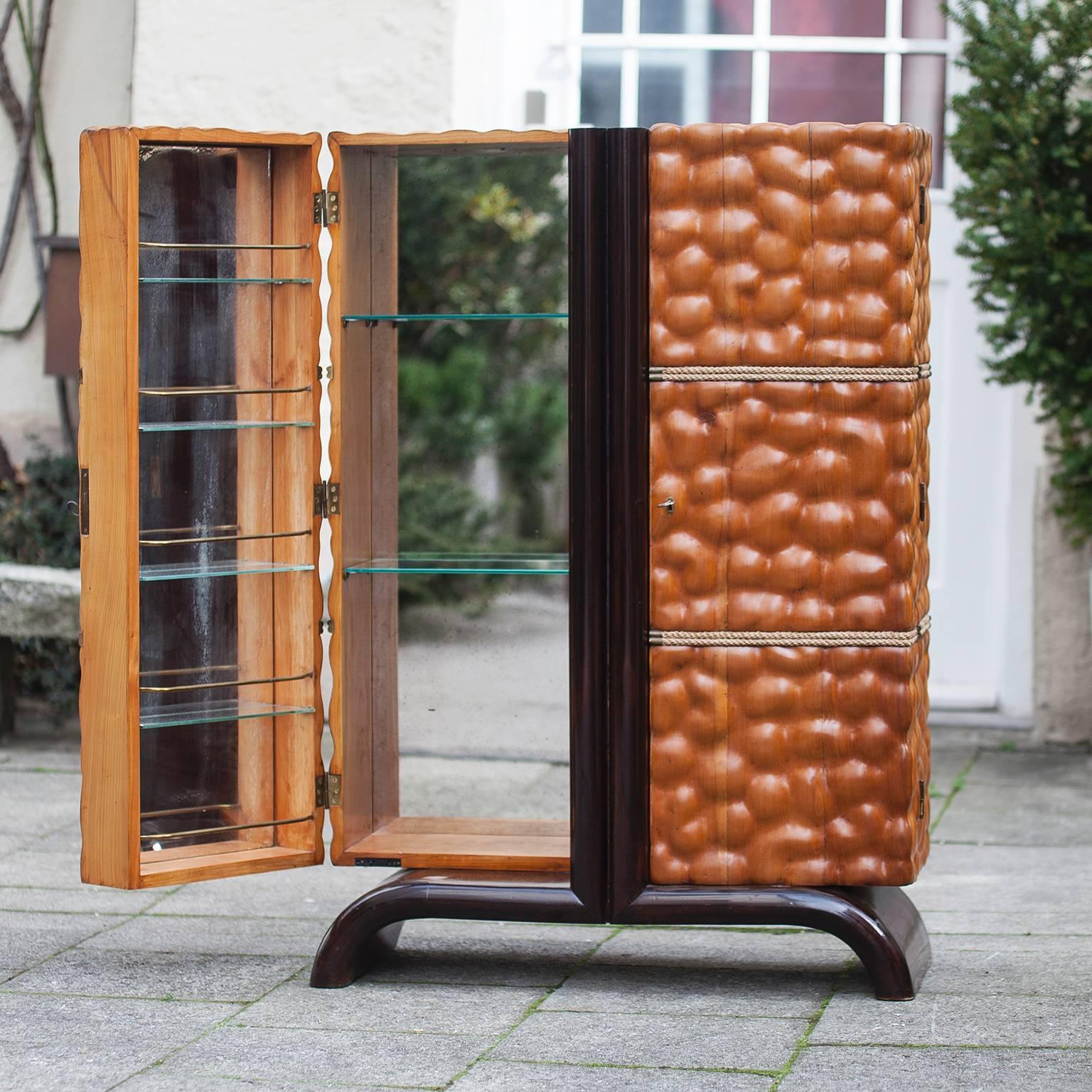 A rare and early cocktail cabinet, designed by and manufactured by Aldo Tura.
Italy, circa 1940, carved cherry, dark stained cherry, polished, decorated with bands of twisted rope, mirrored interior, brass rods, glass shelves, lighting, with a key.