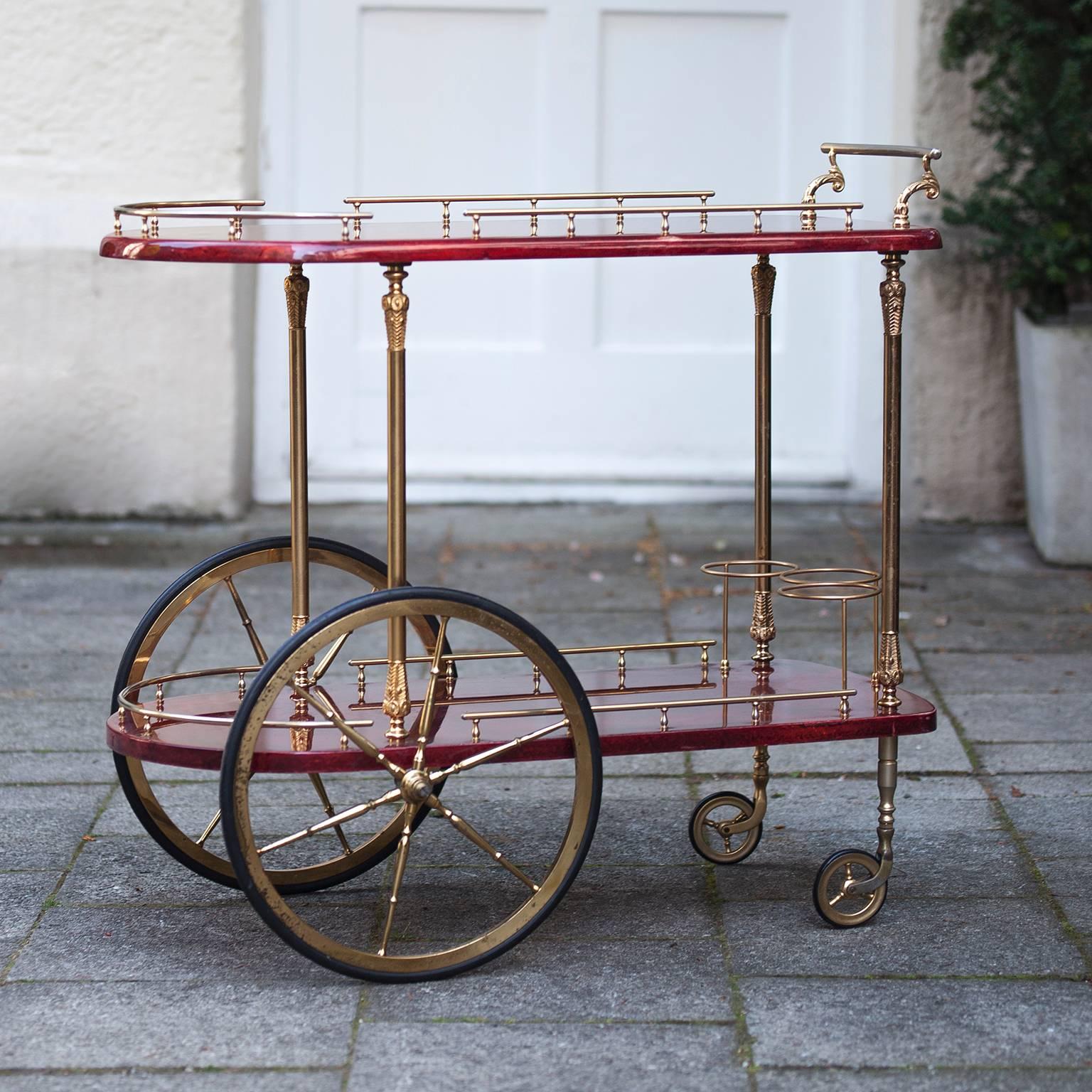 Colorful Italian service and bar cart by Aldo Tura, produced circa 1950s with two rounded tiers in red lacquered goatskin, each with brass galleries, the top with scrolled push handle, the bottom with three bottle holders on spoke wheels, separated