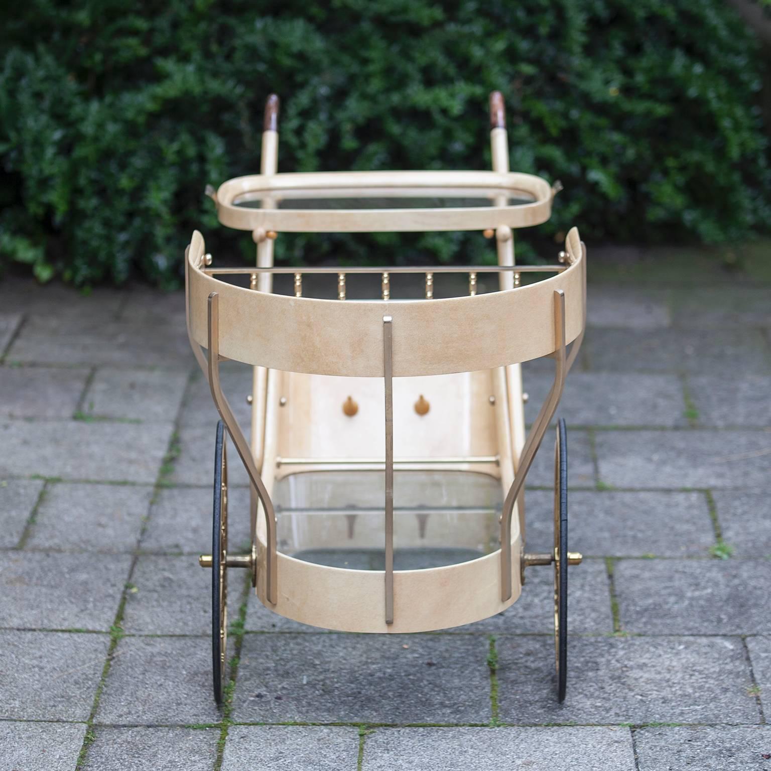 Gorgeous Aldo Tura Hollywood Regency style bar or serving cart by Aldo Tura, Milano, Italy, 1965. Creme lacquered goatskin bar or serving cart with two glass tops and serving tray with brass handles. Original brass wheels and brass applications.