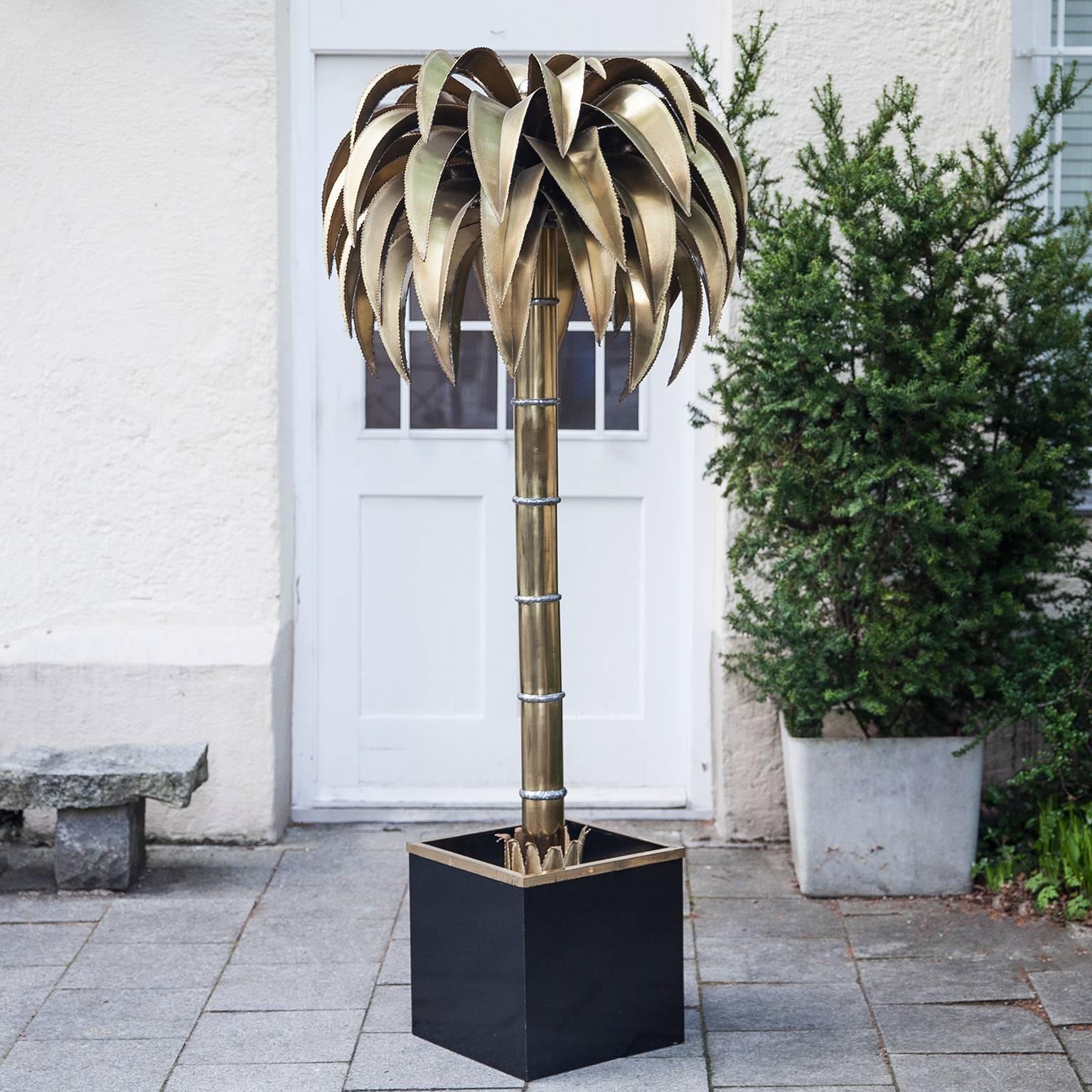 Gorgeous palm tree floor lamp in the Hollywood Regency style, made by Maison Jansen, France, 1960s. Shaped like a palm tree with solid brass leaves and stem, four sockets inside and one uplight, planted in a black square jardiniere. 
An elegant