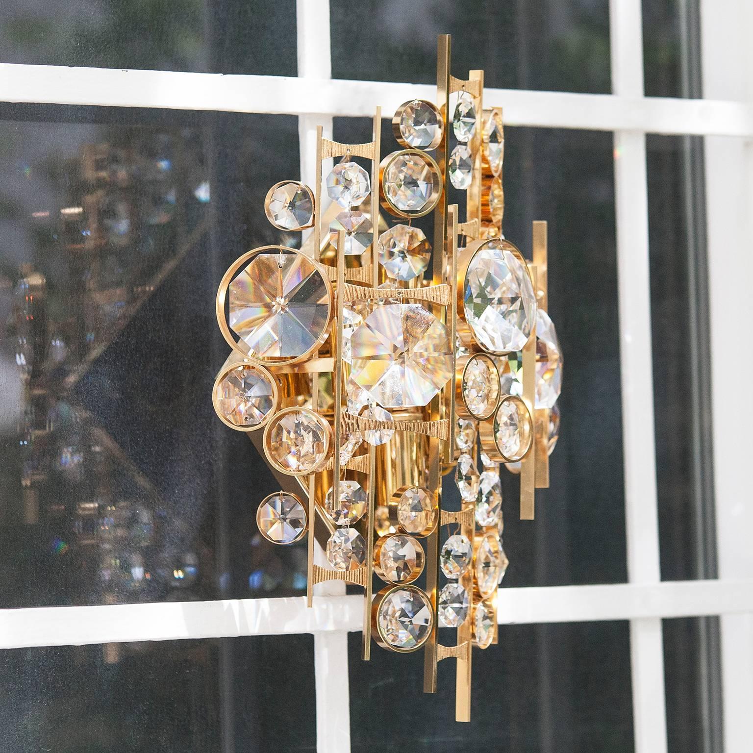 Gorgeous Hollywood Regency style wall light in gilt brass and with over 50 glass crystals made by Palwa, Austria, 1960s. 
This Hollywood Regency crystal glass disc sconces, has a frame of real gilt metal. It needs four x E14 standard screw bulbs to