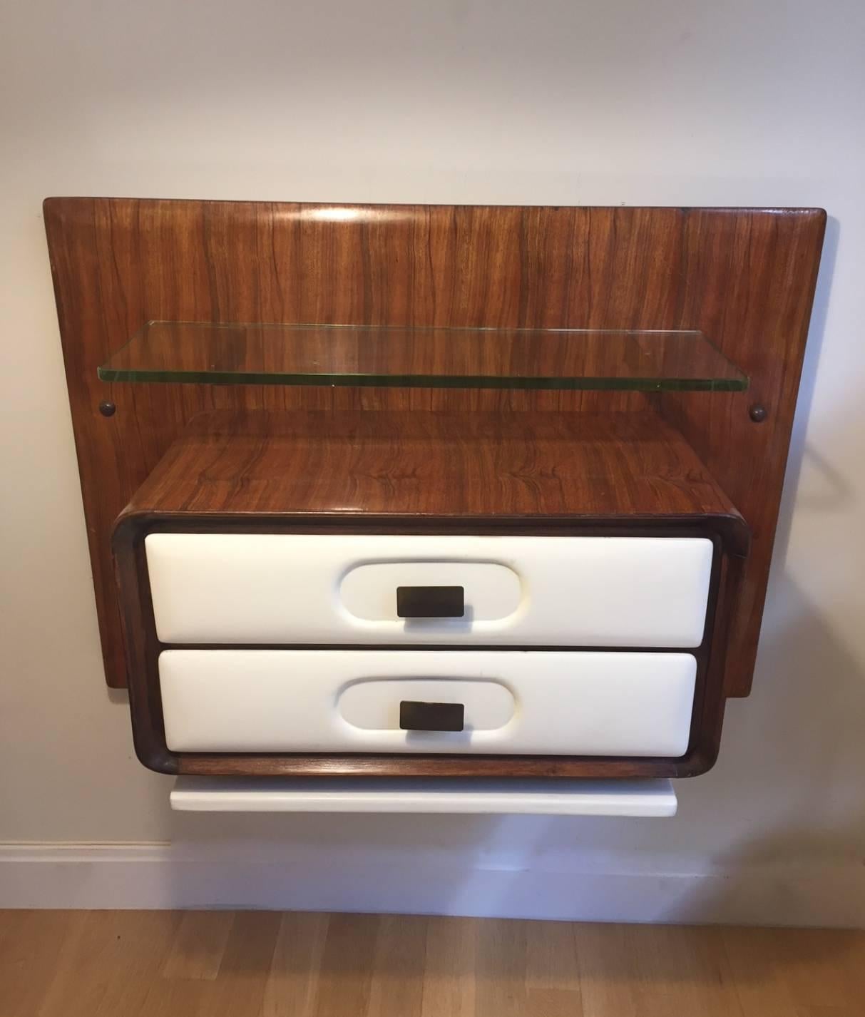 A pair of wall-mounted nightstands designed by Melchiore Vega in the 1960s. Mongoy wood wood, top glass and two white lacquered drawers with brass handles. Excellent condition.

 