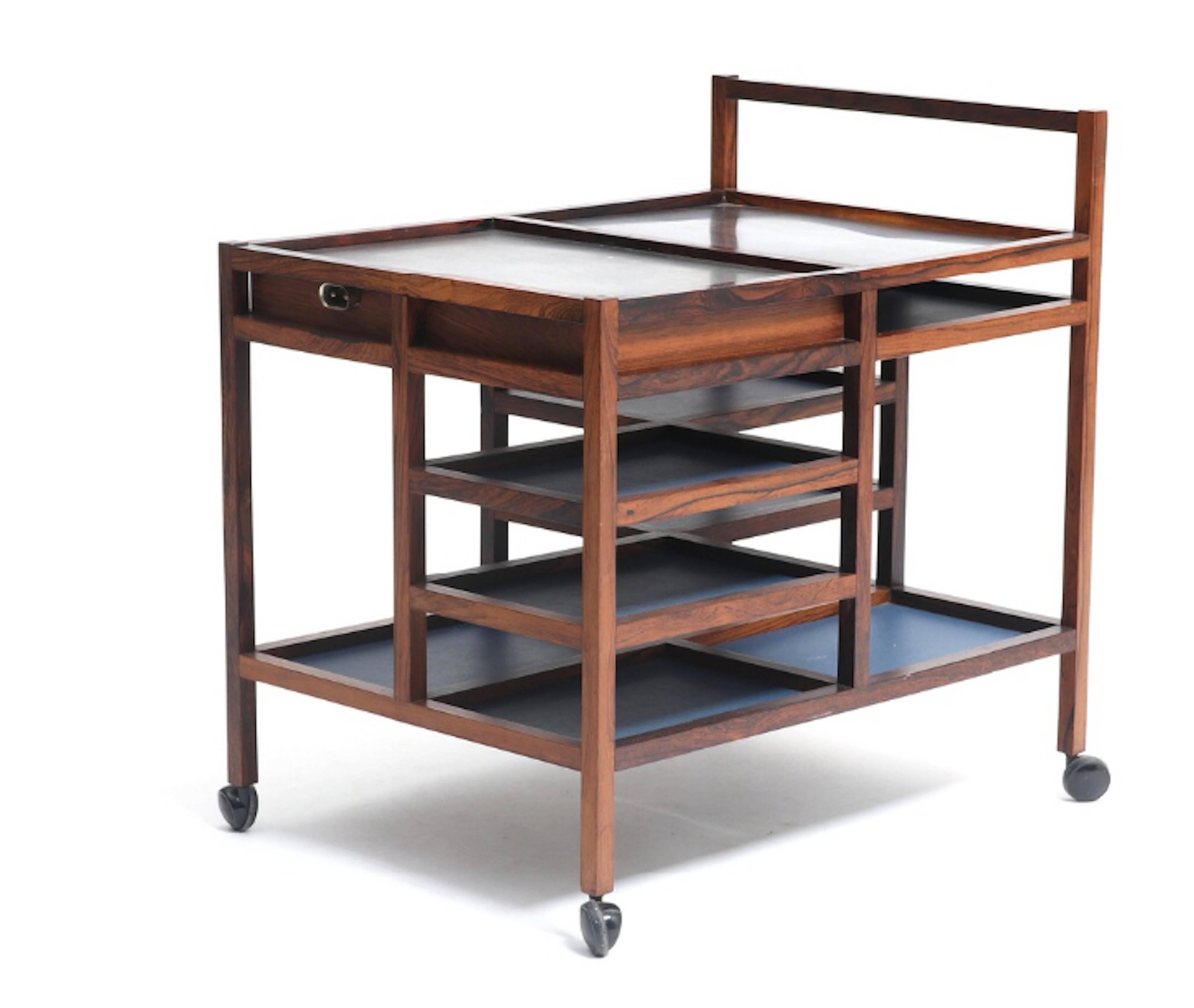 A Brazilian rosewood serving cart .Top in two sections with steel, one with electric heating. One drawer and shelves covered with blue vinyl. Mounted on casters. This piece edited late 1960s by Pedersen & and Son.
Bodil Kjaer designed this serving